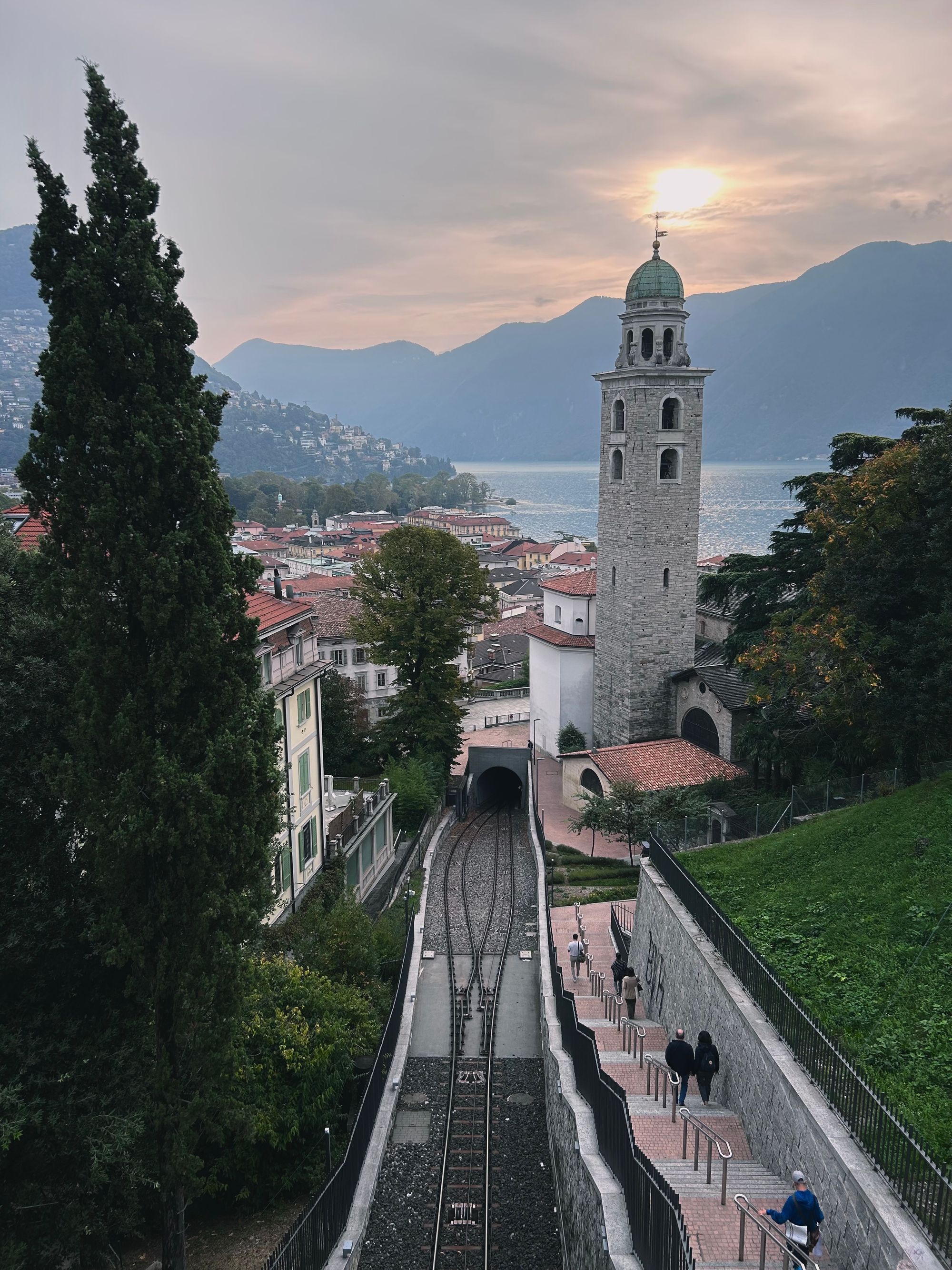 view of Lugao from the train platform: bell tower, railway tracks with town and lake as the backdrop, mid-morning.