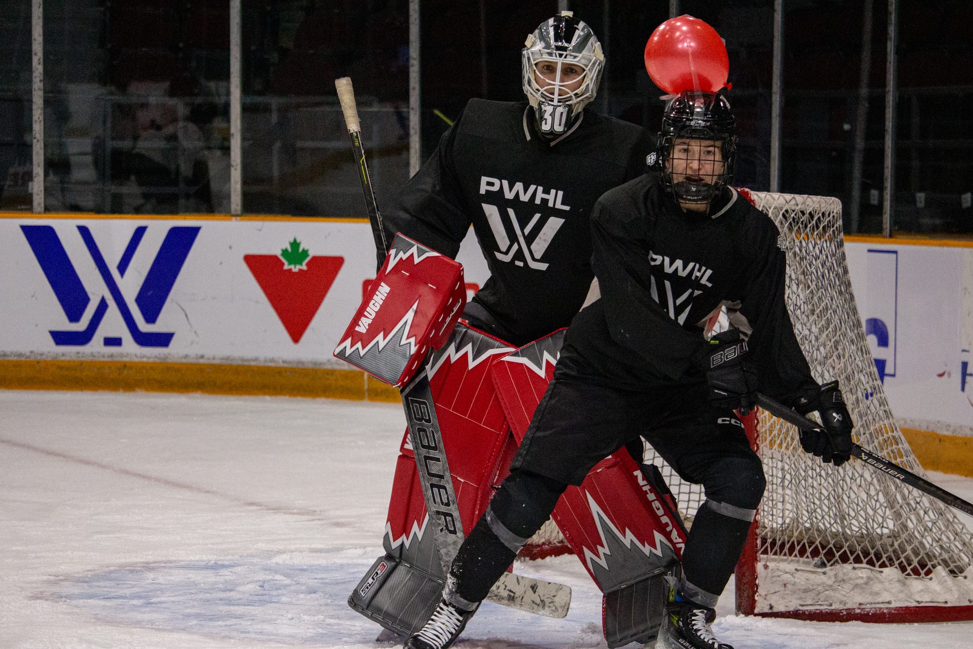 Aneta Tejralová skates in front of goalie Sandra Abstreiter. Tejralová has a red balloon taped to her helmet. 