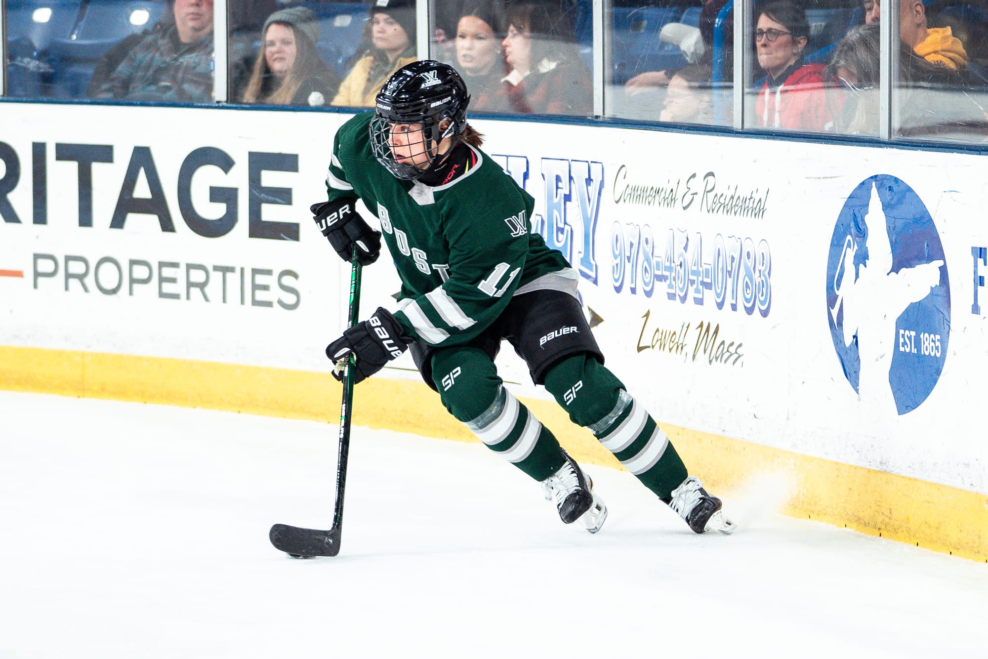 Alina Müller, wearing a green home uniform, skates with the puck during a game. 