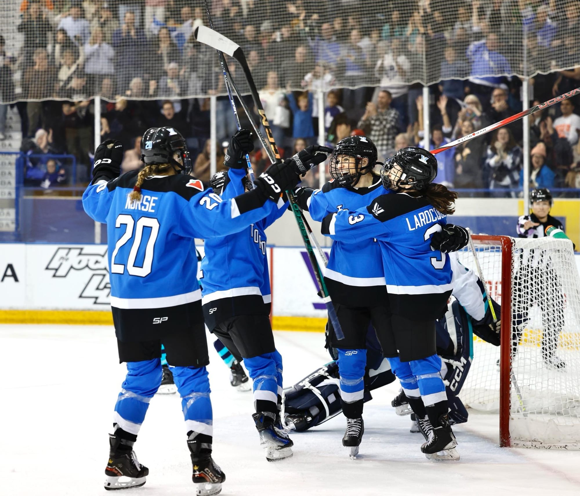 Natalie Spooner celebrates her goal with her teammates, all wearing blue home uniforms.