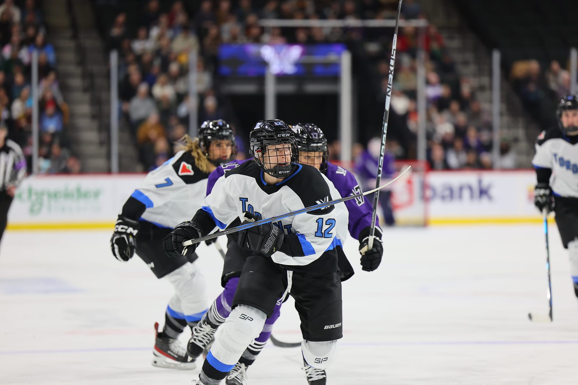 Allie Monroe, wearing a white away uniform, races for the puck against Minnesota's Brooke Bryant, wearing a purple away uniform.. 