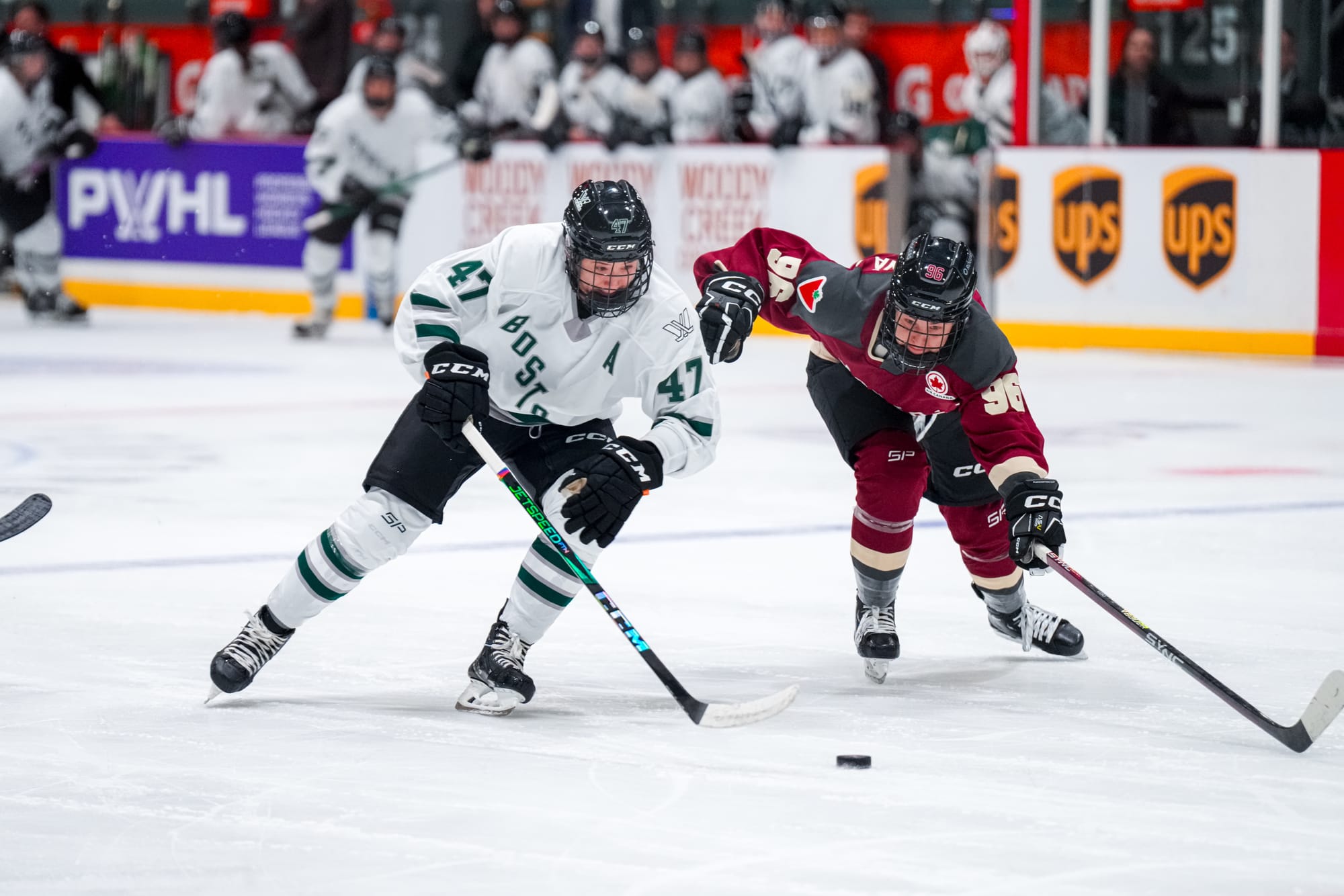 Jamie Lee Rattray, in a white away uniform protects the puck from Montréal's Dominika Lásková, wearing a maroon home uniform.