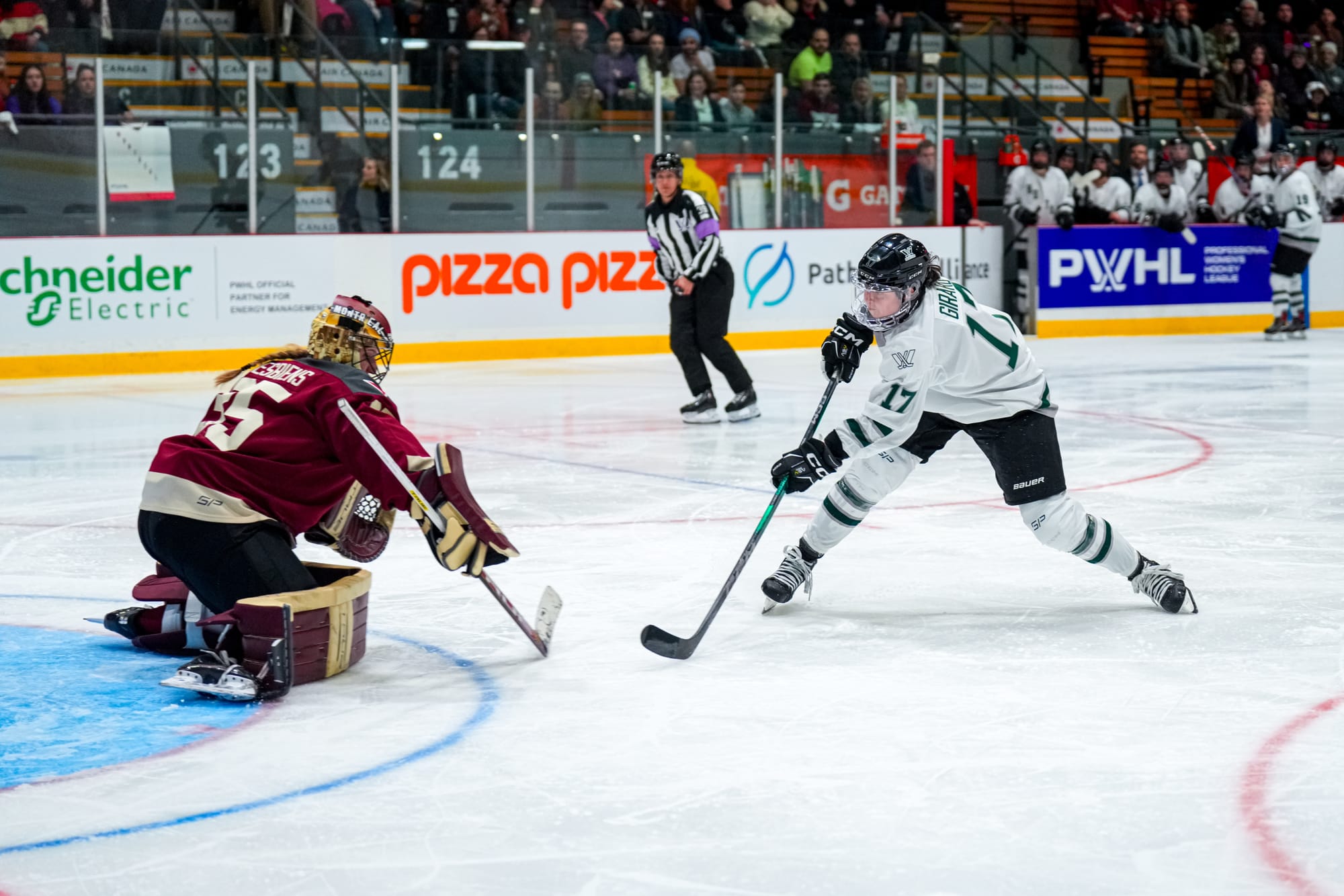 Taylor Girard, wearing a white home uniform, takes a shot on Ann-Renée Desbiens, wearing a maroon home uniform and her Montréal mask and pads.. 