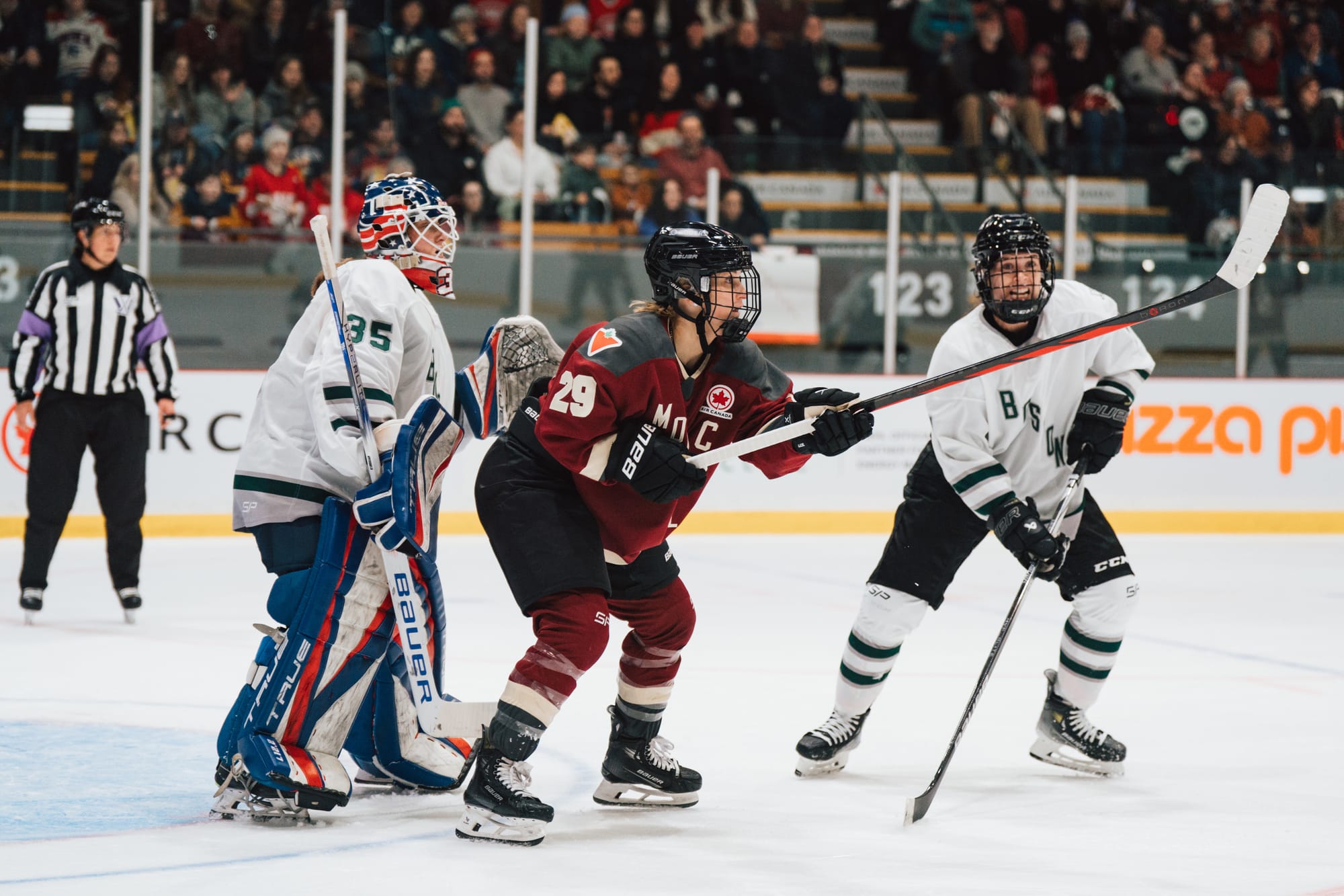 Marie-Philip Poulin, wearing a maroon home uniform, tries to settle the puck in front of Aerin Frankel, wearing a white away uniform and her USA gear.