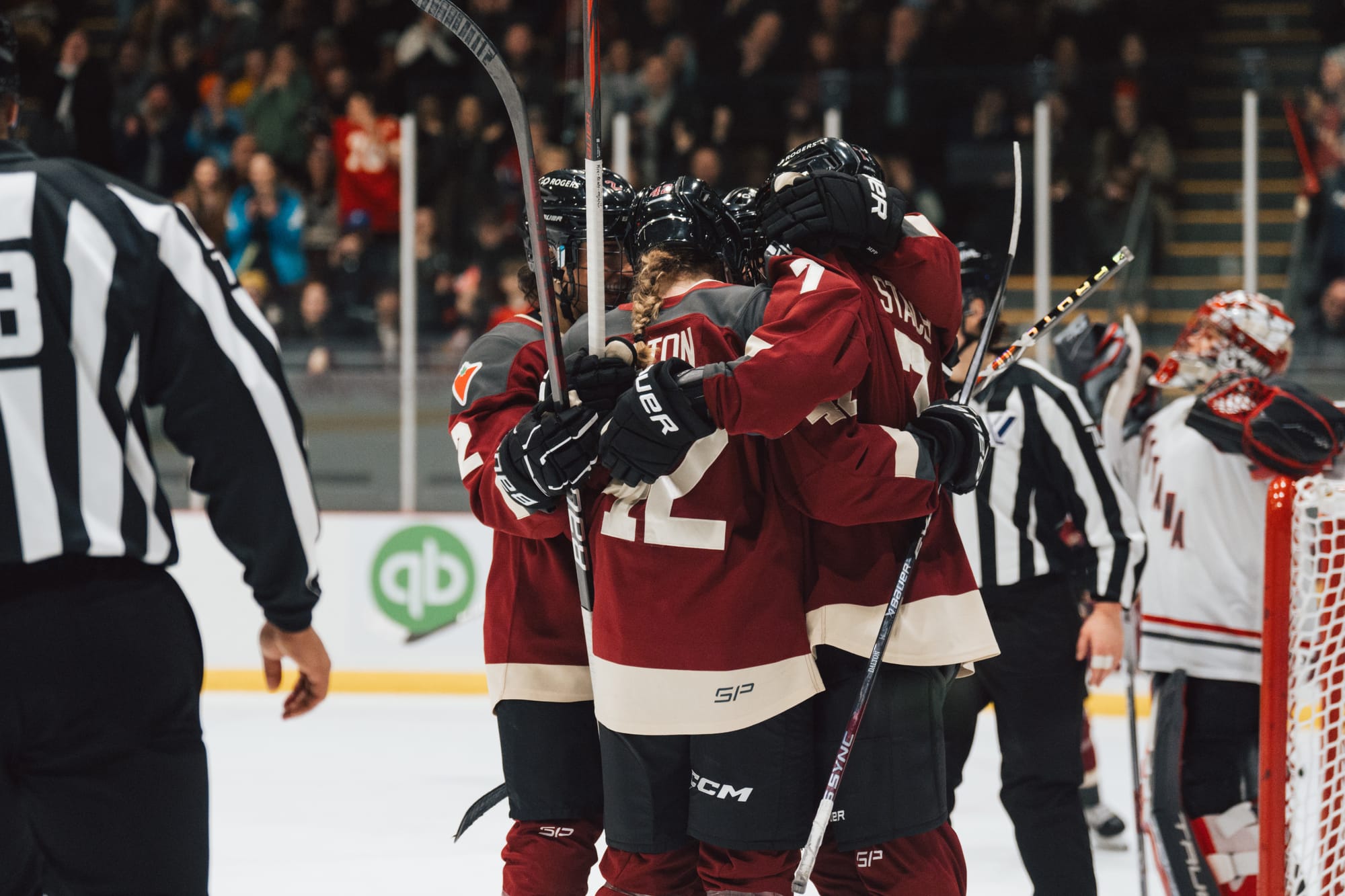 Claire Dalton celebrates one of her goals against Ottawa with her teammates. They are in a group hug and wearing their maroon home uniforms.