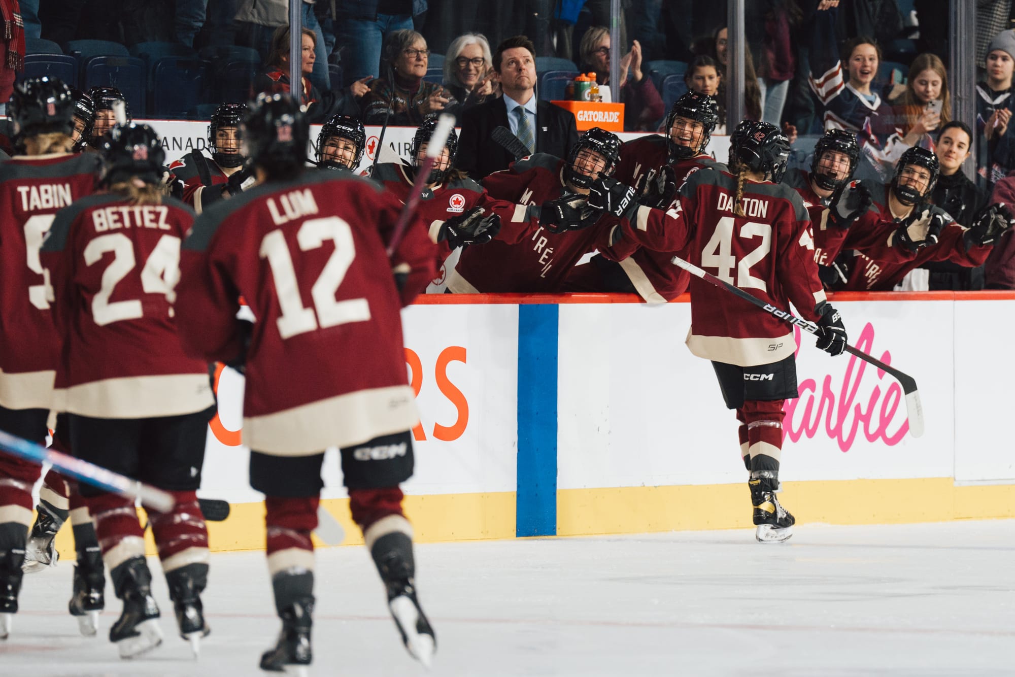 Claire Dalton, wearing a maroon home jersey, celebrates her goal against Minnesota at the bench. 