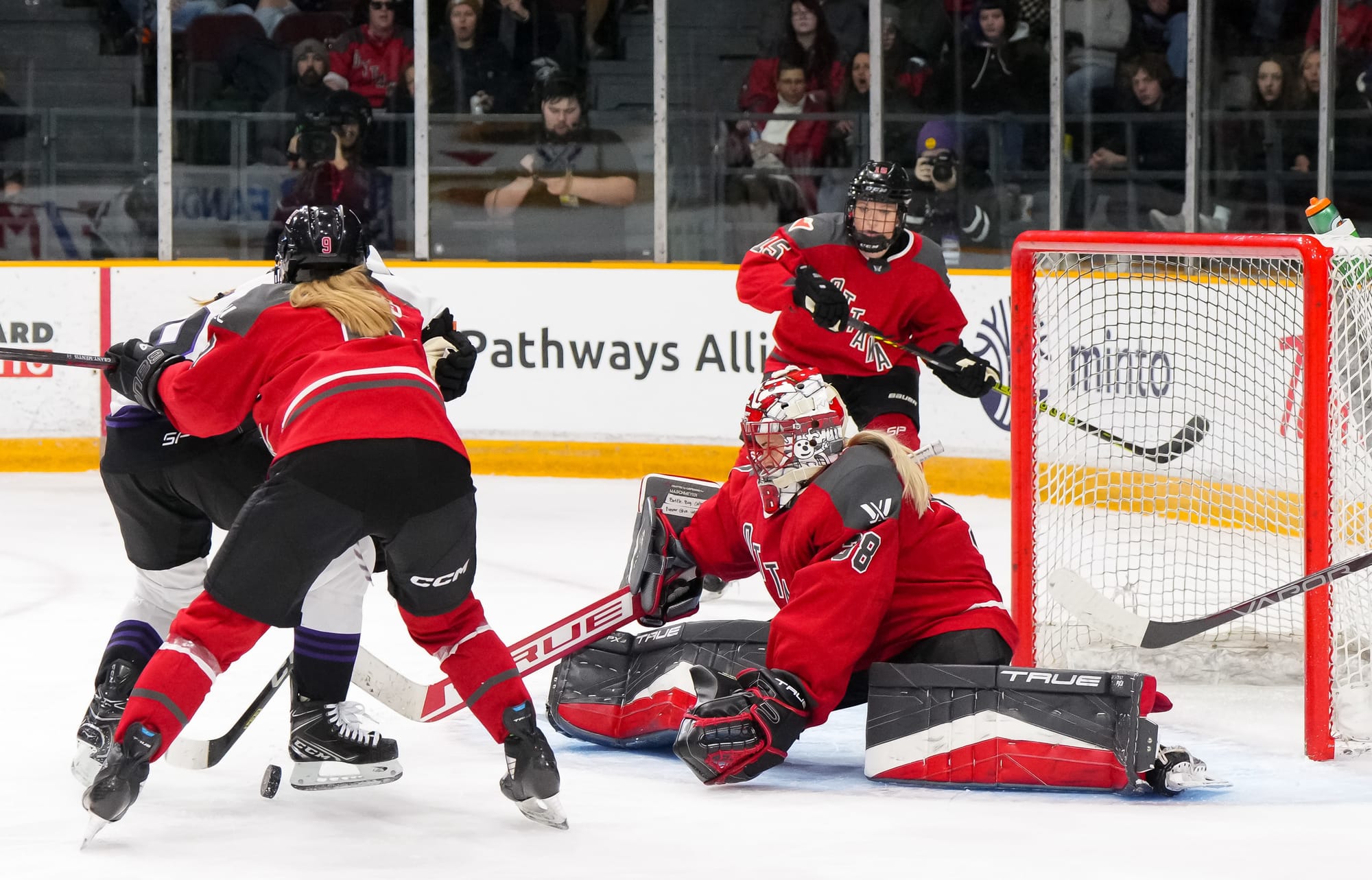 Emerance Maschmeyer, wearing a red home jersey, black and red gear, and her Ottawa mask, makes a save against Minnesota. 
