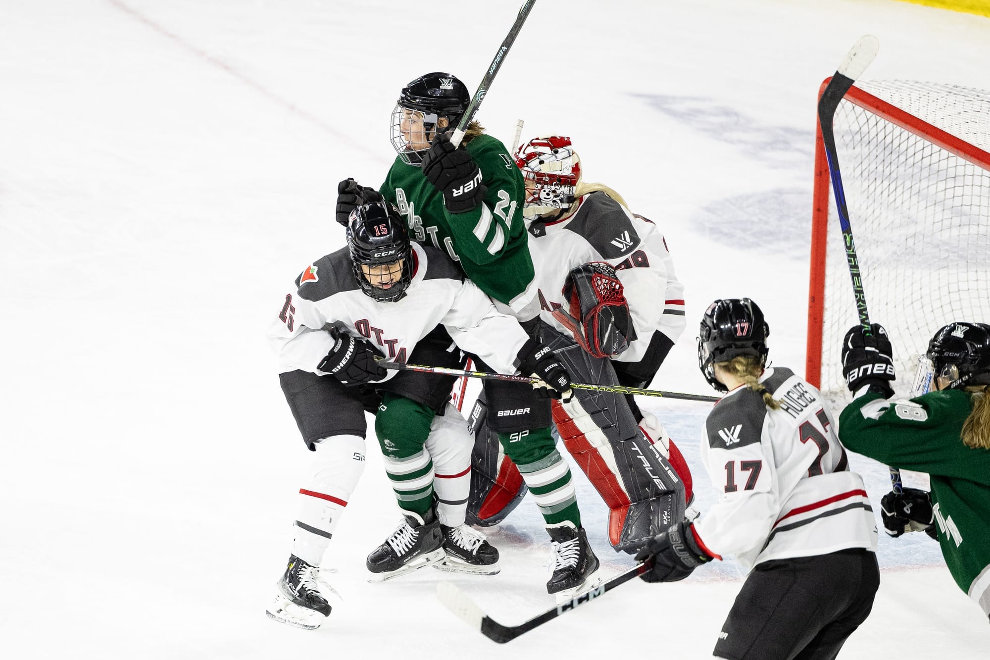 Hilary Knight screens Emerance Maschmeyer while Savannah Harmon tries to push her out of the way. Knight is in green, and Maschmeyer and Harmon are in white. 