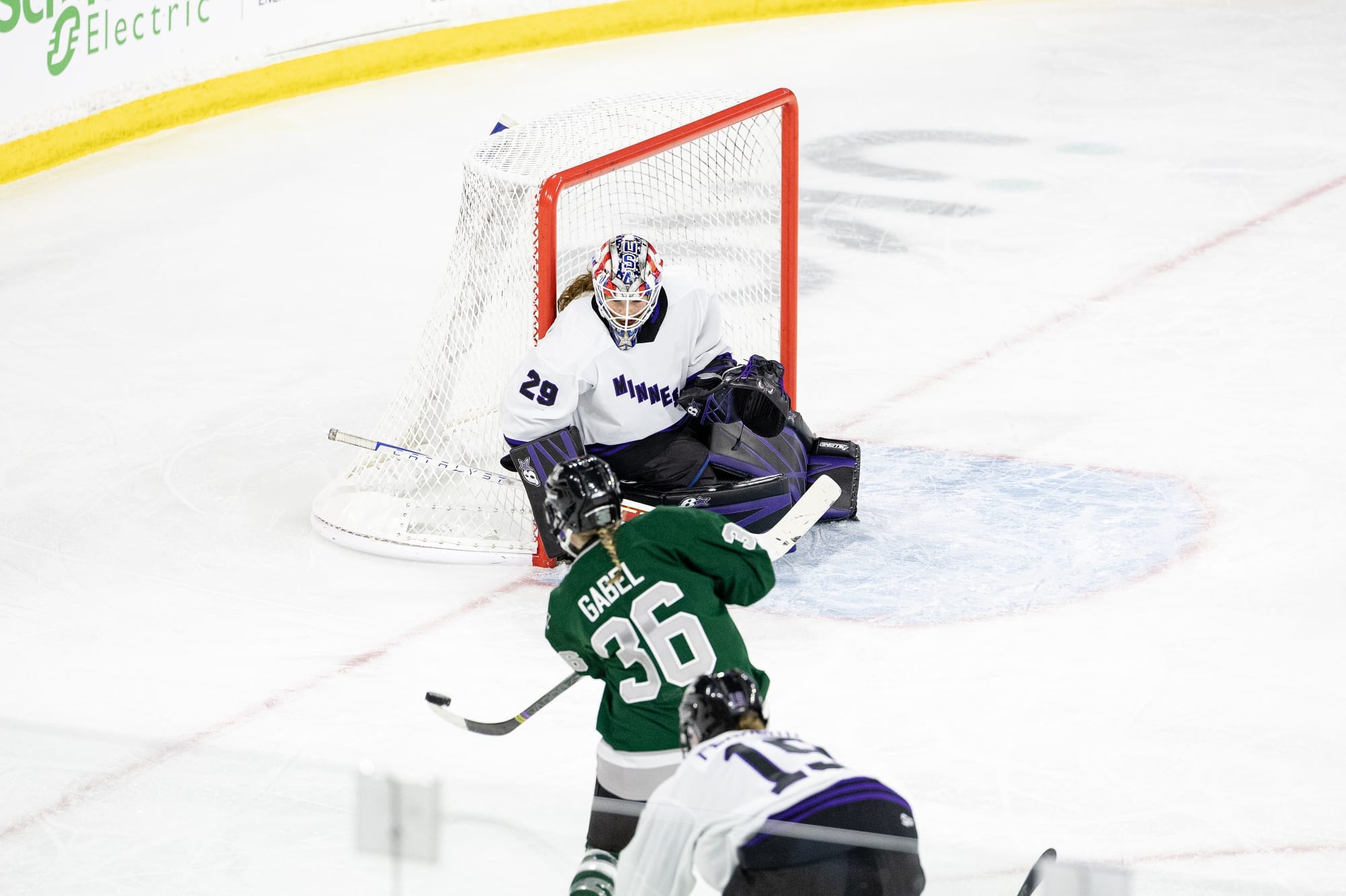 Loren Gabel shoots on Nicole Hensley. Gabel is wearing a green home uniform, while Hensley is in a white away uniform with her purple Minnesota pads but red/white/blue USA mask.