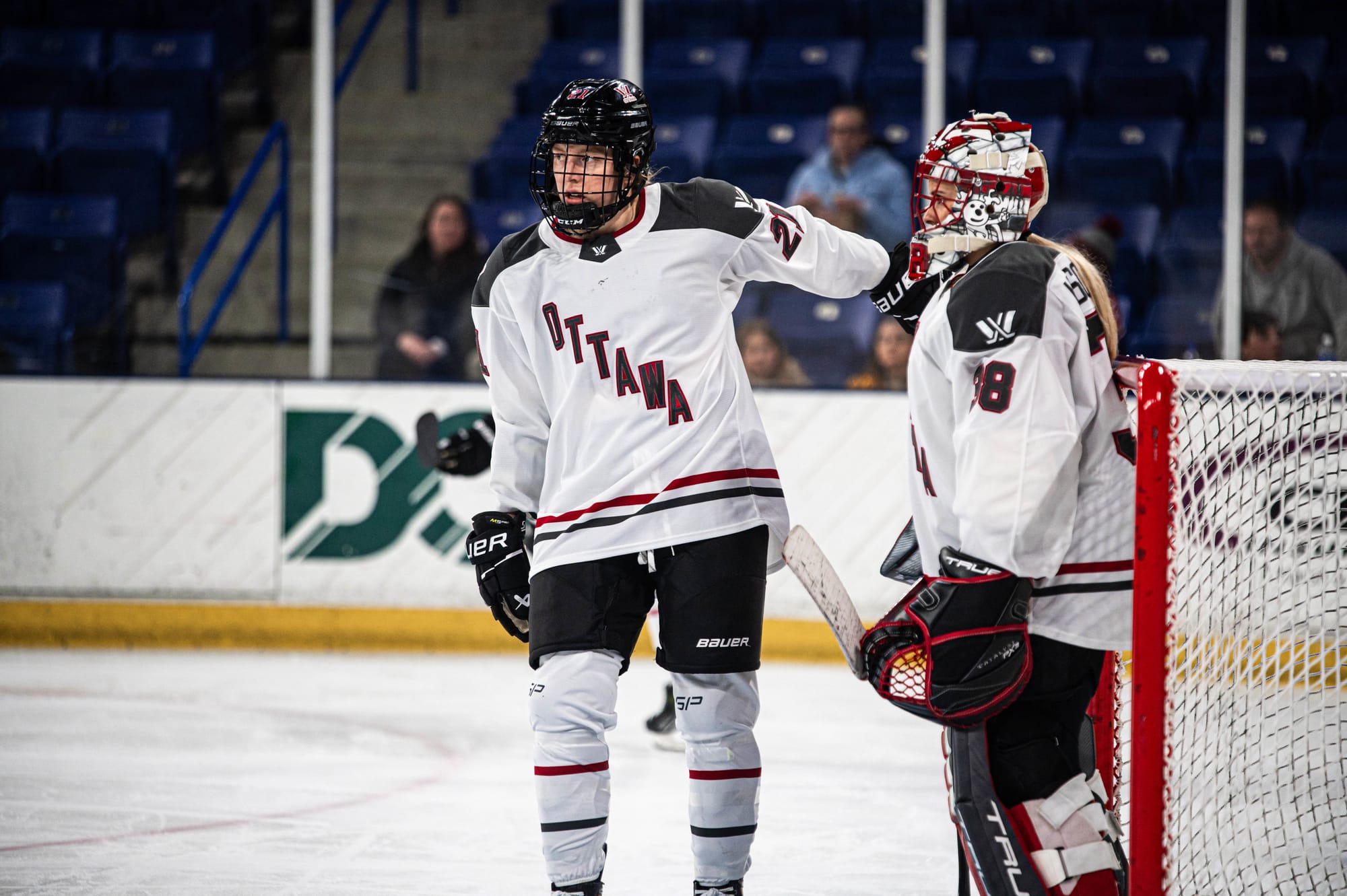 Ashton Bell pats Emerance Maschmeyer on the shoulder. Both players are wearing white away uniforms. Maschmeyer is also wearing are red/white Ottawa Mask and black/red/white pads.