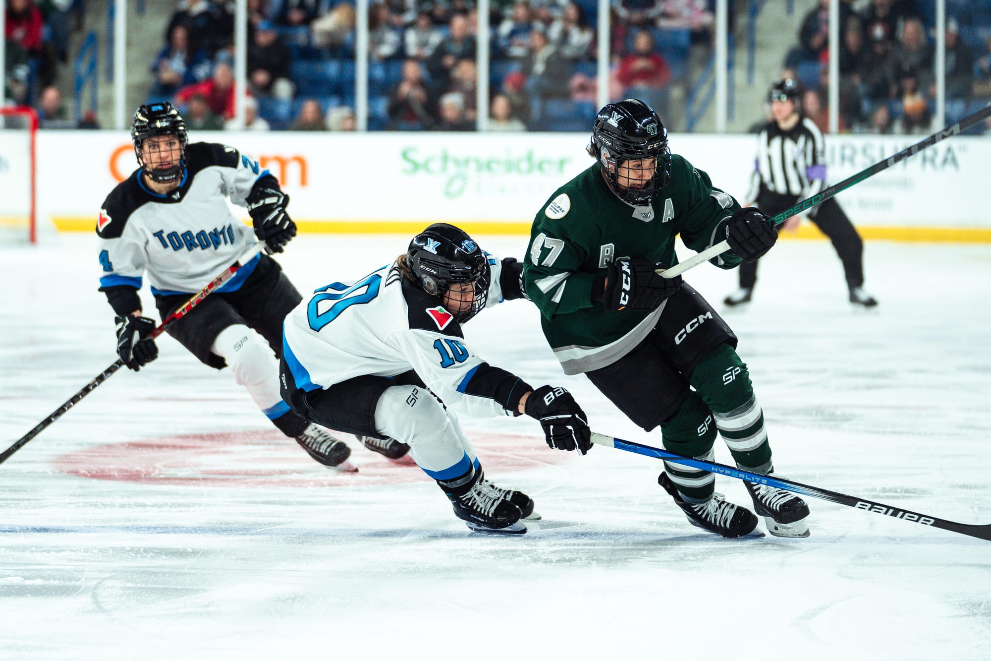 Alex Vasko pokes the puck away from Jamie Lee Rattray. Rattray is trying to get body positioning on Vasko, as Vasko lunges forward to poke the puck. Vasko is in white, while Rattray is in green.