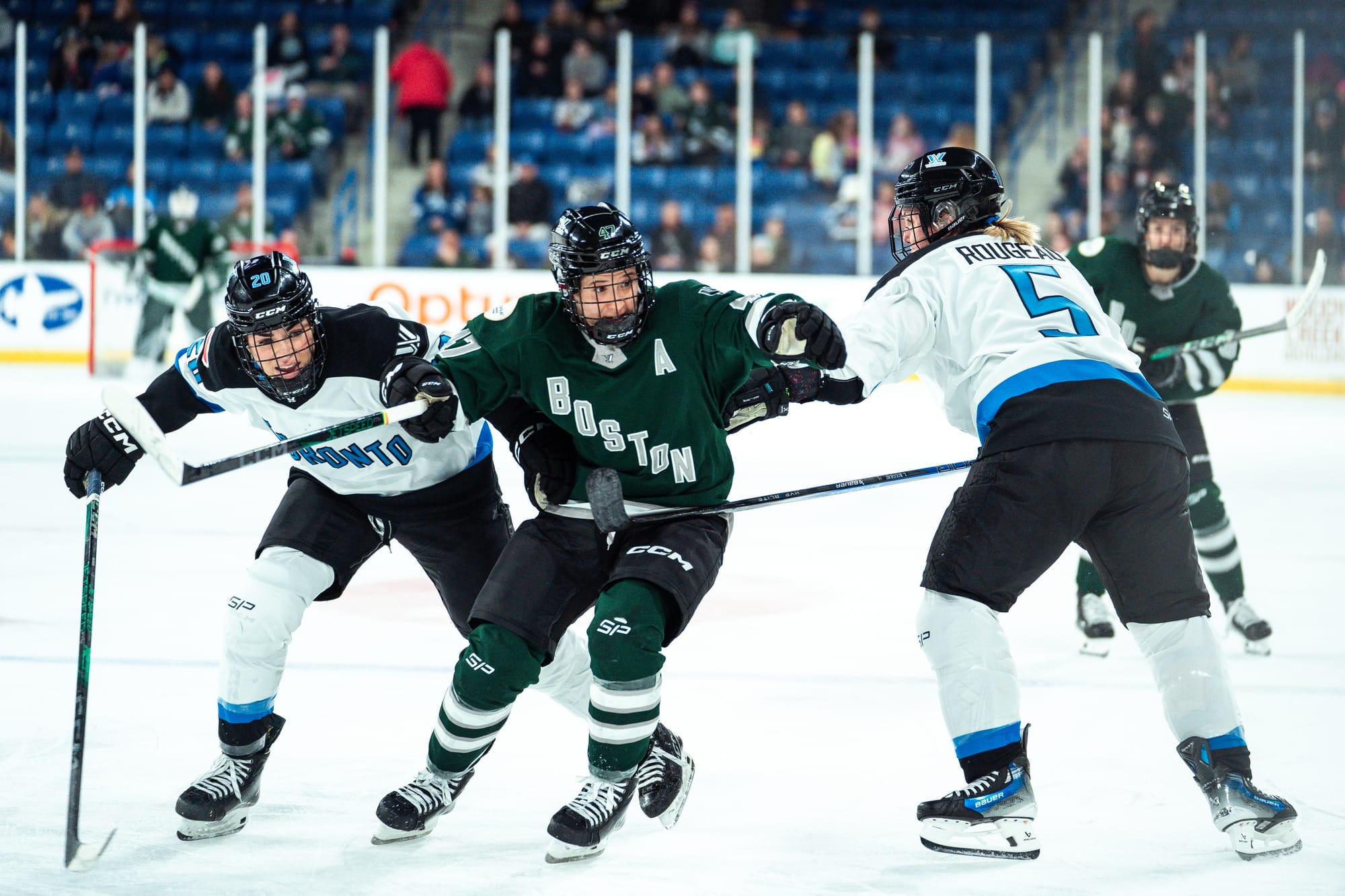 Jamie Lee Rattray hunts the puck as Toronto players try to defend her. She skating in between Sarah Nurse, who is chasing her, and Lauriane Rougeau, who is skating backwards defending. Rattray is in green, while the Toronto players are in white