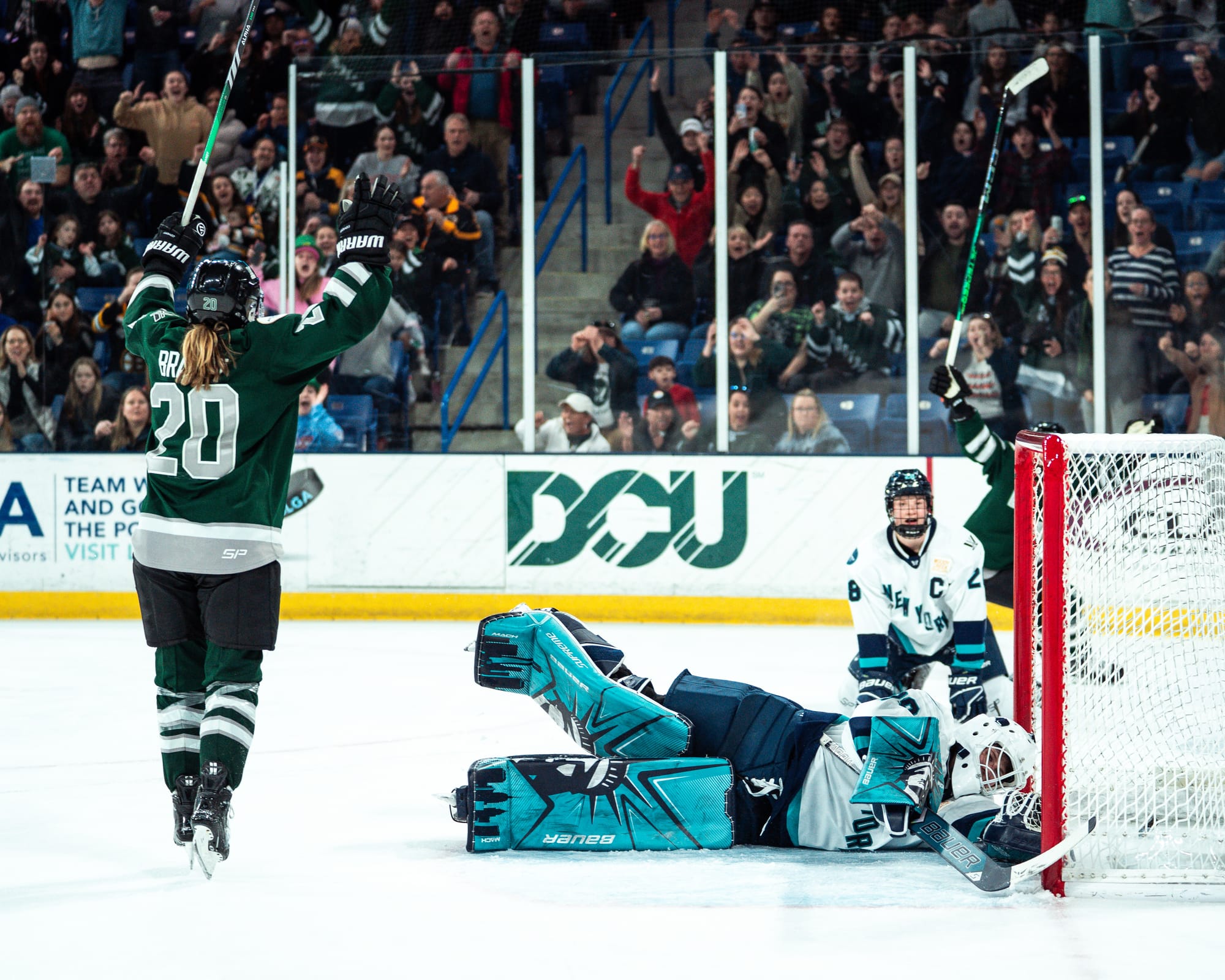 New York players sit in dismay after losing in overtime to Boston. Abbey Levy is laying flat after trying to make a save, while Micah Zandee-Hart is on her knees behind her. Meanwhile, Hannah Brandt is celebrating in front of them after scoring. The New York players are in white, Boston in green.