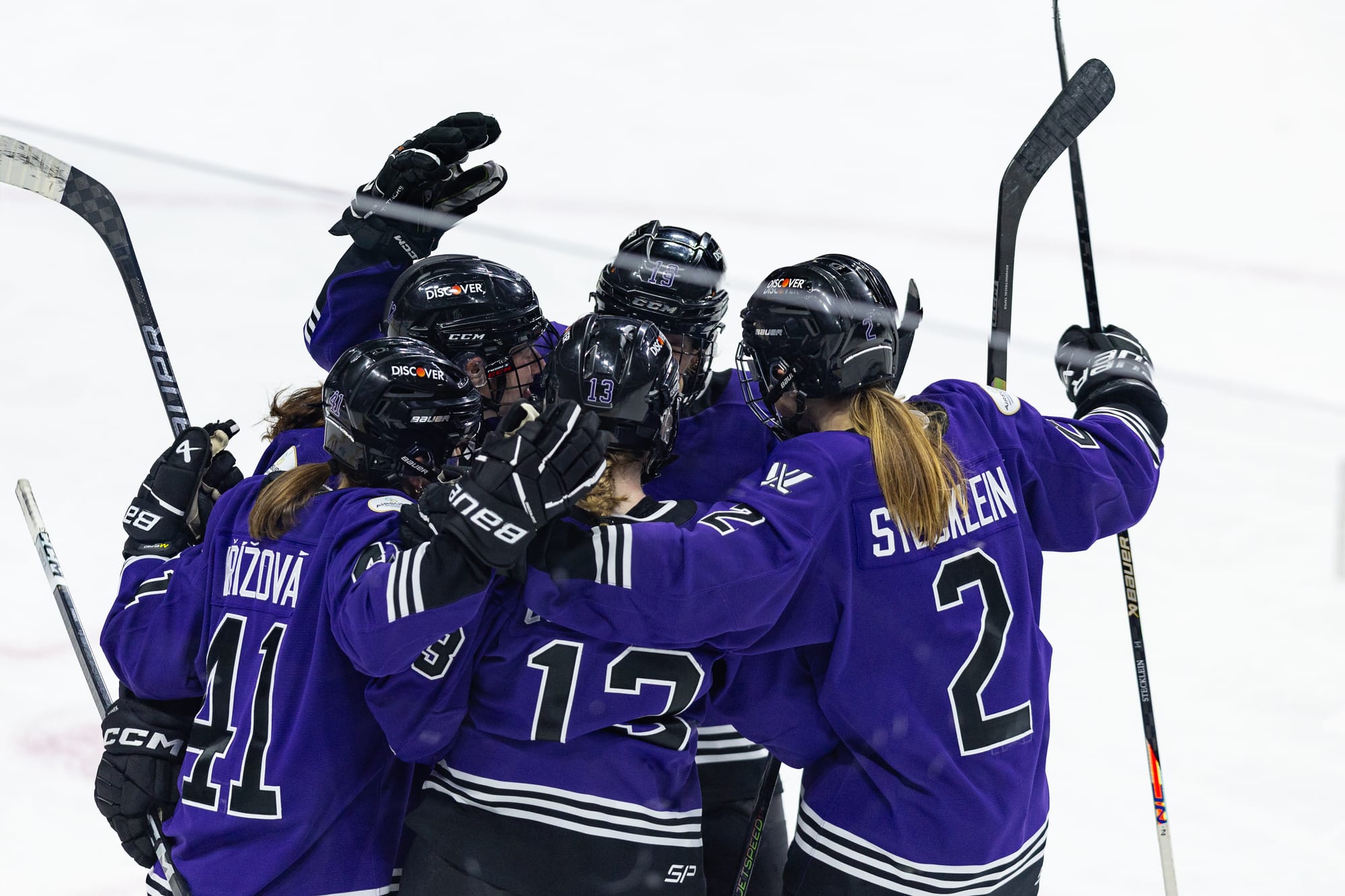 Minnesota players celebrate a goal against Boston. There are five of them in a big group hug. They are all wearing purple home uniforms.
