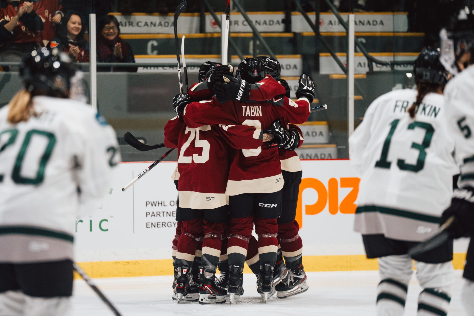 Montréal players celebrate a goal against Boston. They are in a group hug, and all are wearing maroon home uniforms.