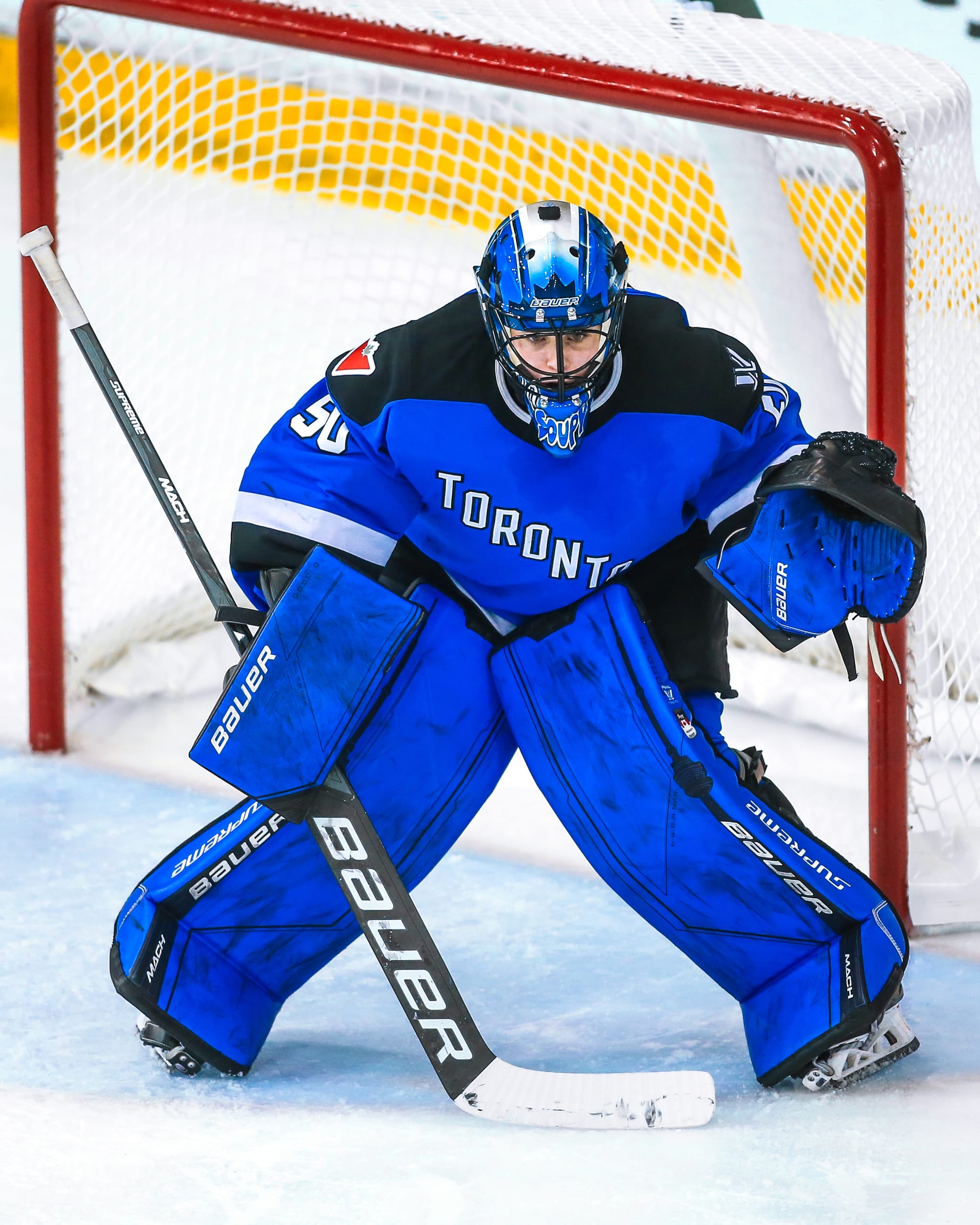 Kristen Campbell prepares to make a save against Boston. She is crouched down with her glove up and ready. She is wearing her blue pads and mask along with her blue home uniform.