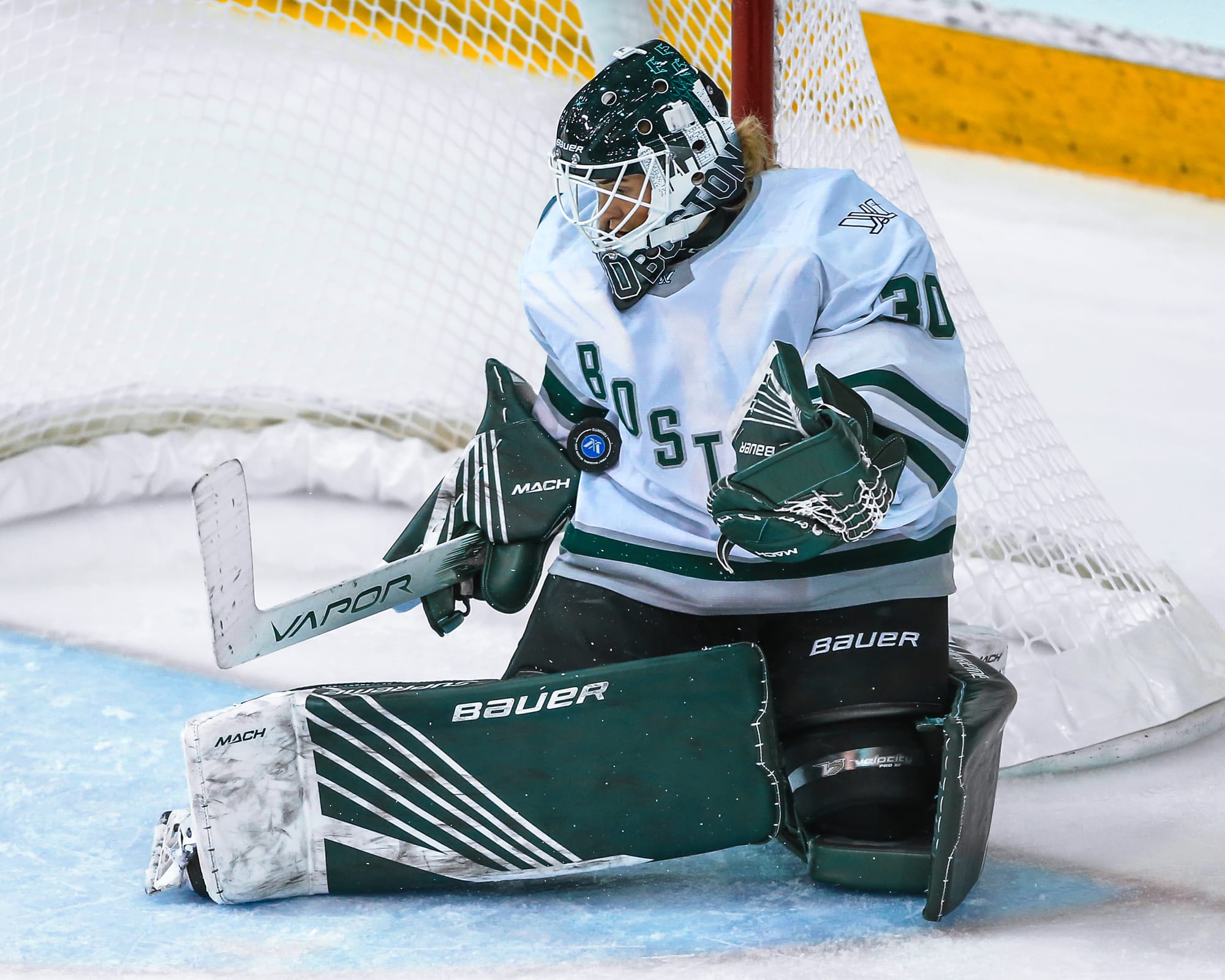 Emma Söderberg makes a save against Toronto. The puck is in her chest. She is wearing a white away uniform and her green Boston gear and mask. 