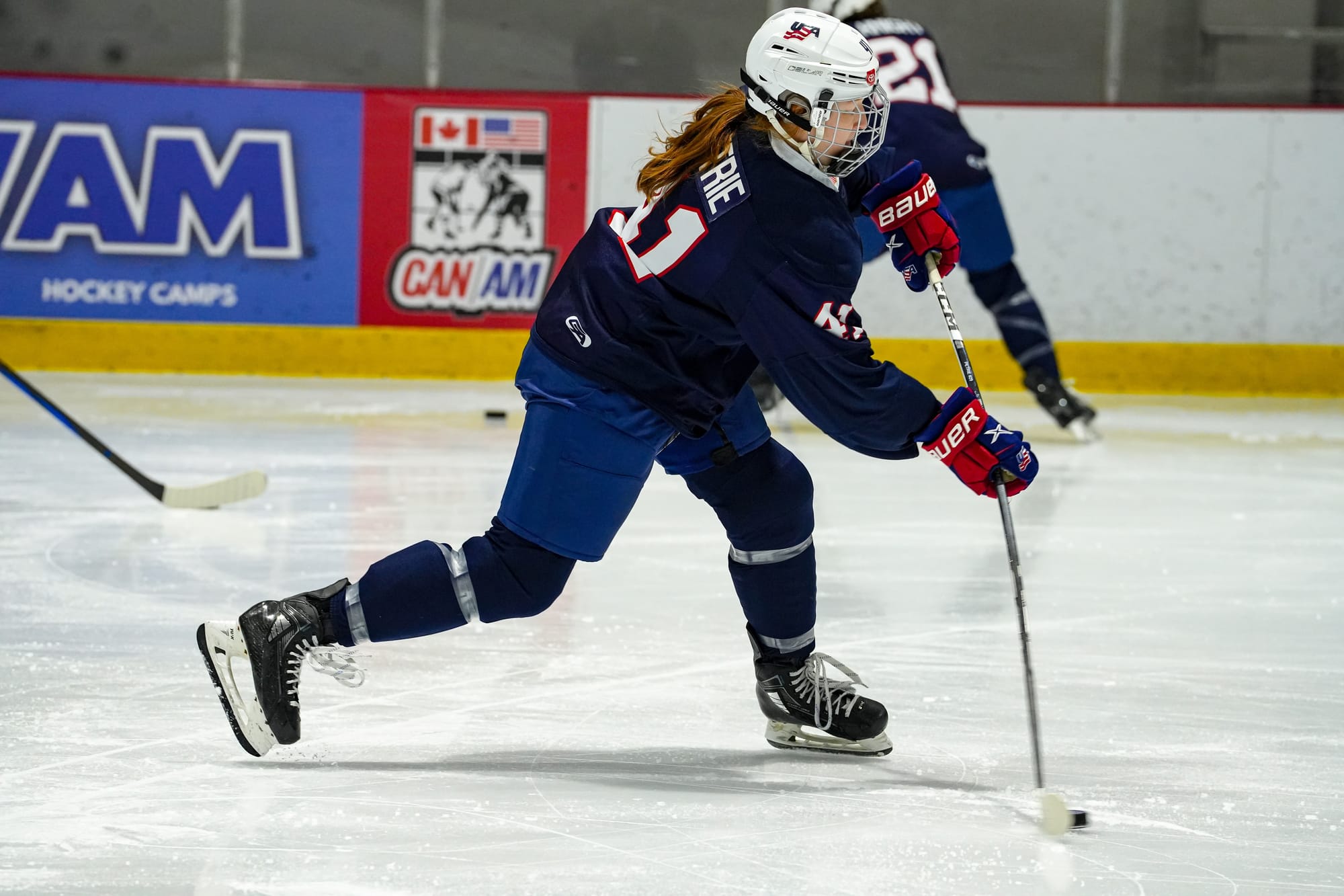 Dominque Petrie takes a shot during warmups before a scrimmage. Her weight is all on her left (front) leg and her stick is bent, as she is in the middle of taking a wrist shot. She is wearing a navy blue uniform.