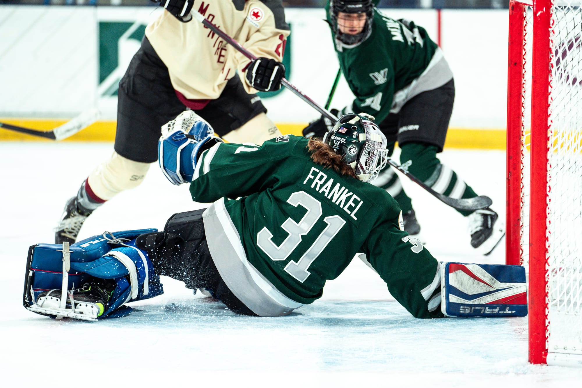 Aerin Frankel makes a diving save against Montréal. She is wearing a green home uniform, green and white Boston mask, and red/white/blue pads.
