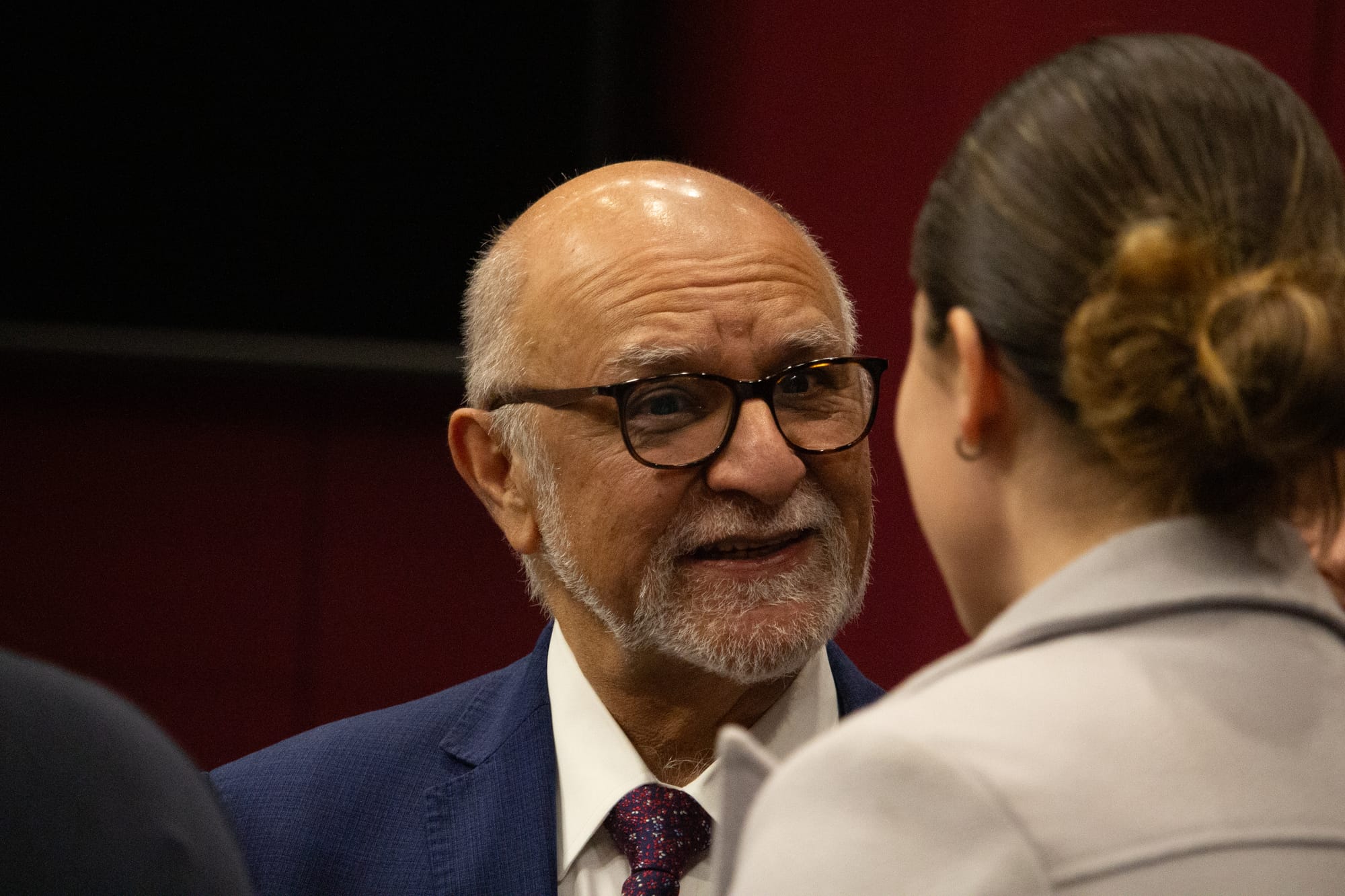 A senator wearing glasses speaks with a woman.