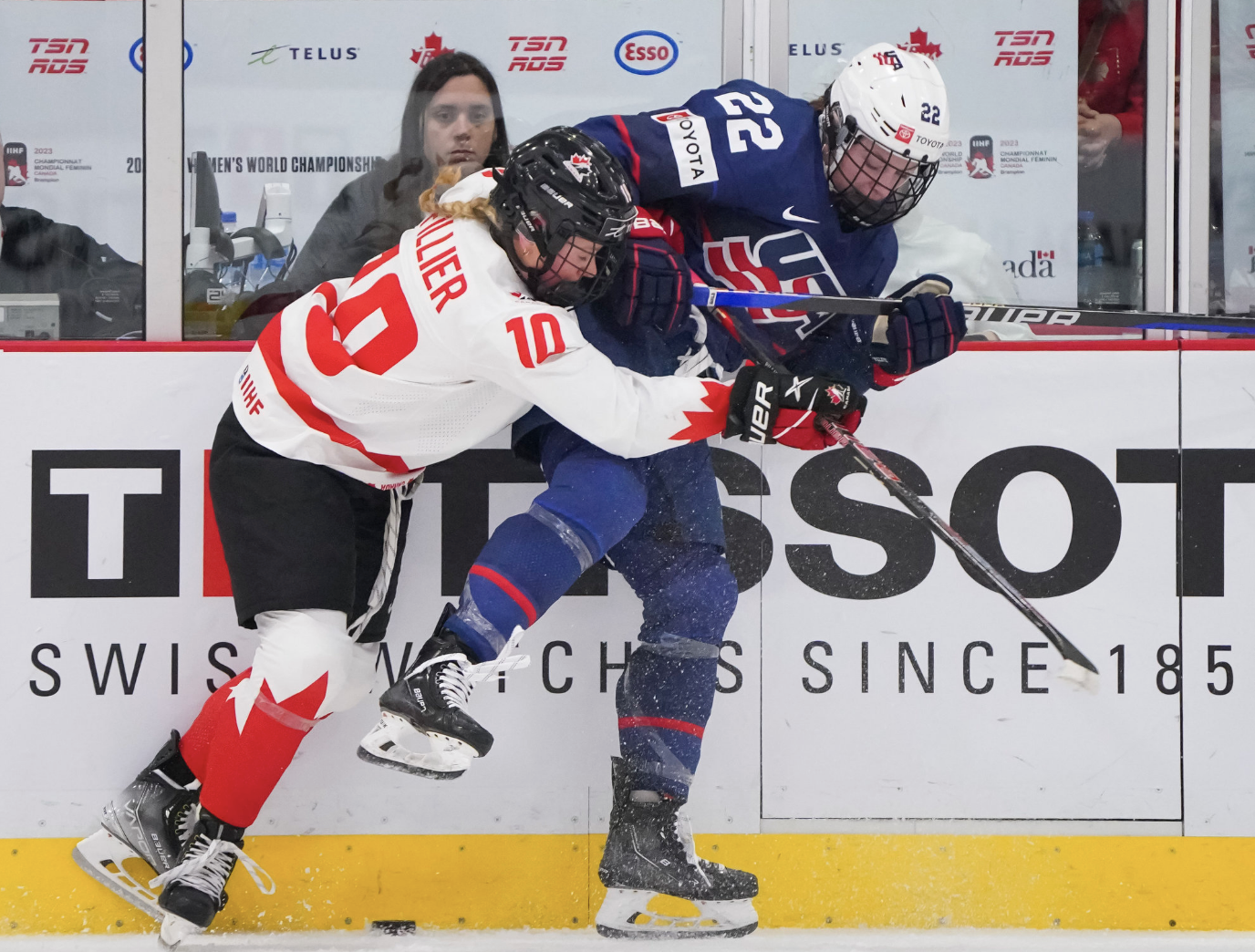 Fillier (left in white) hits Janecke (right in navy) along the boards. Fillier is more hunched over than Janceke, whose right leg is in the air. The puck is in between them. 