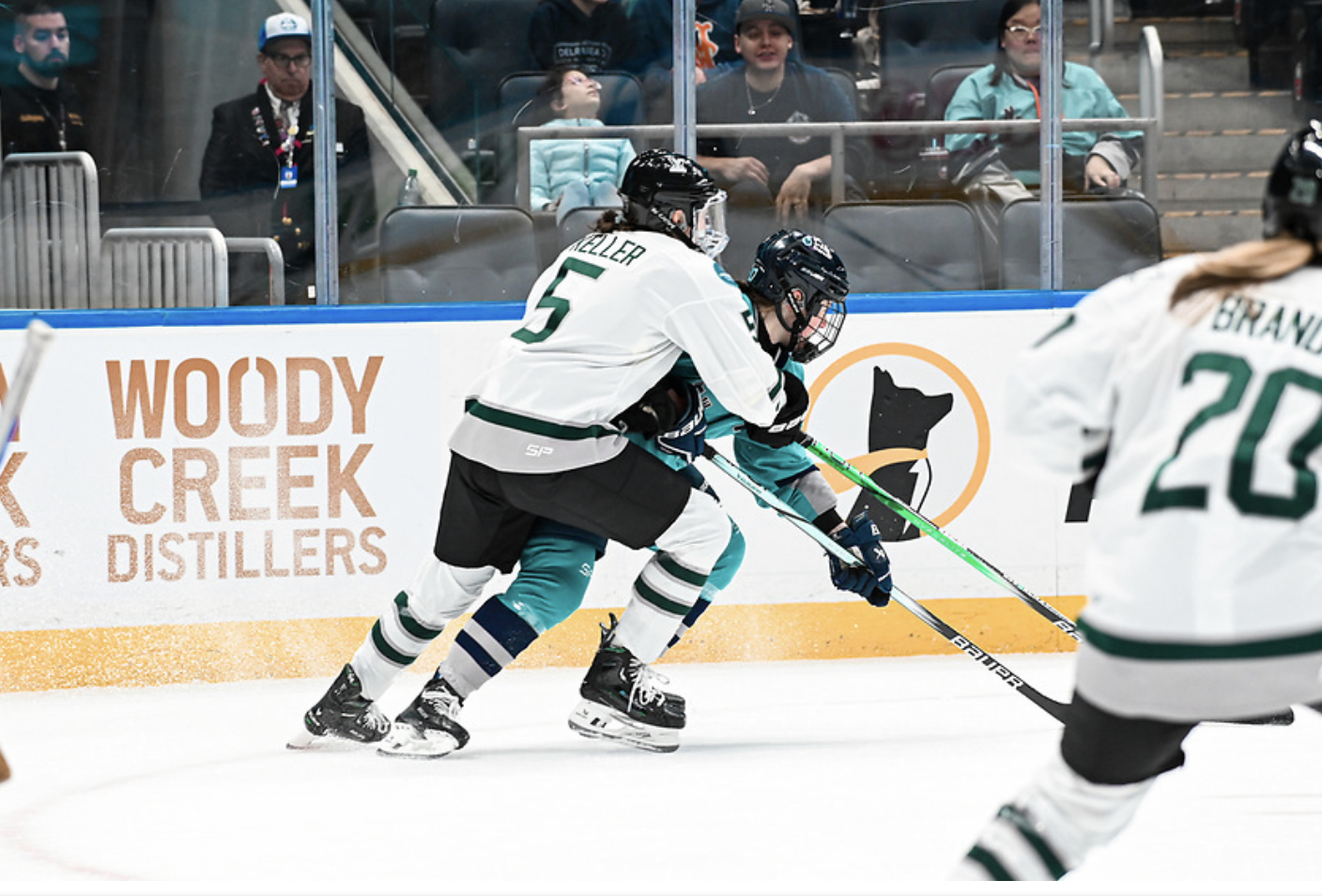 Megan Keller defends against a New York skater. Keller is wrapped around the New York player from behind, and the puck is out of view. Keller is white, while the New York player is in teal.