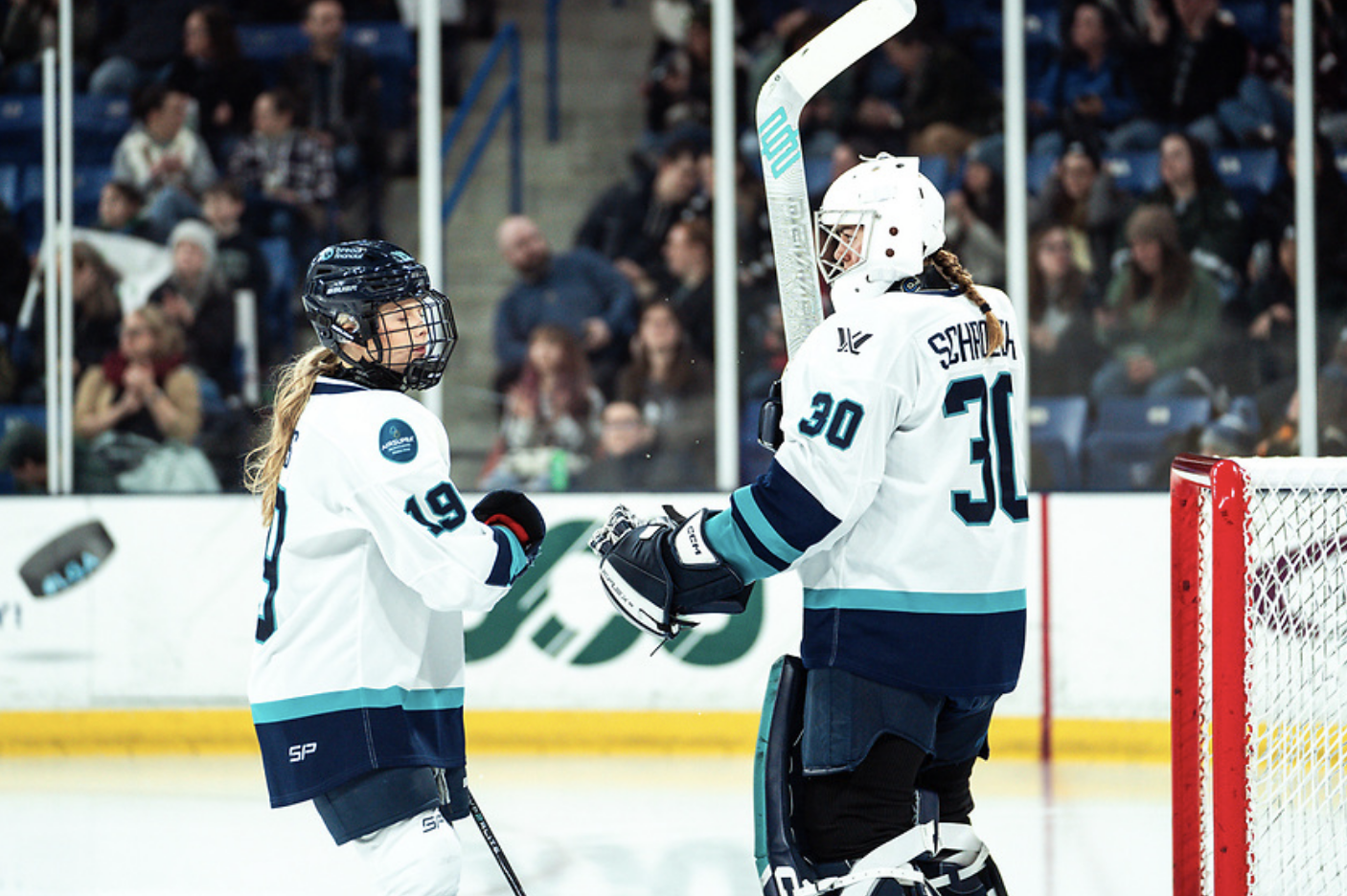 Levis (left) fist bumps Schroeder (right) in front of the net. Both are in white away uniforms.