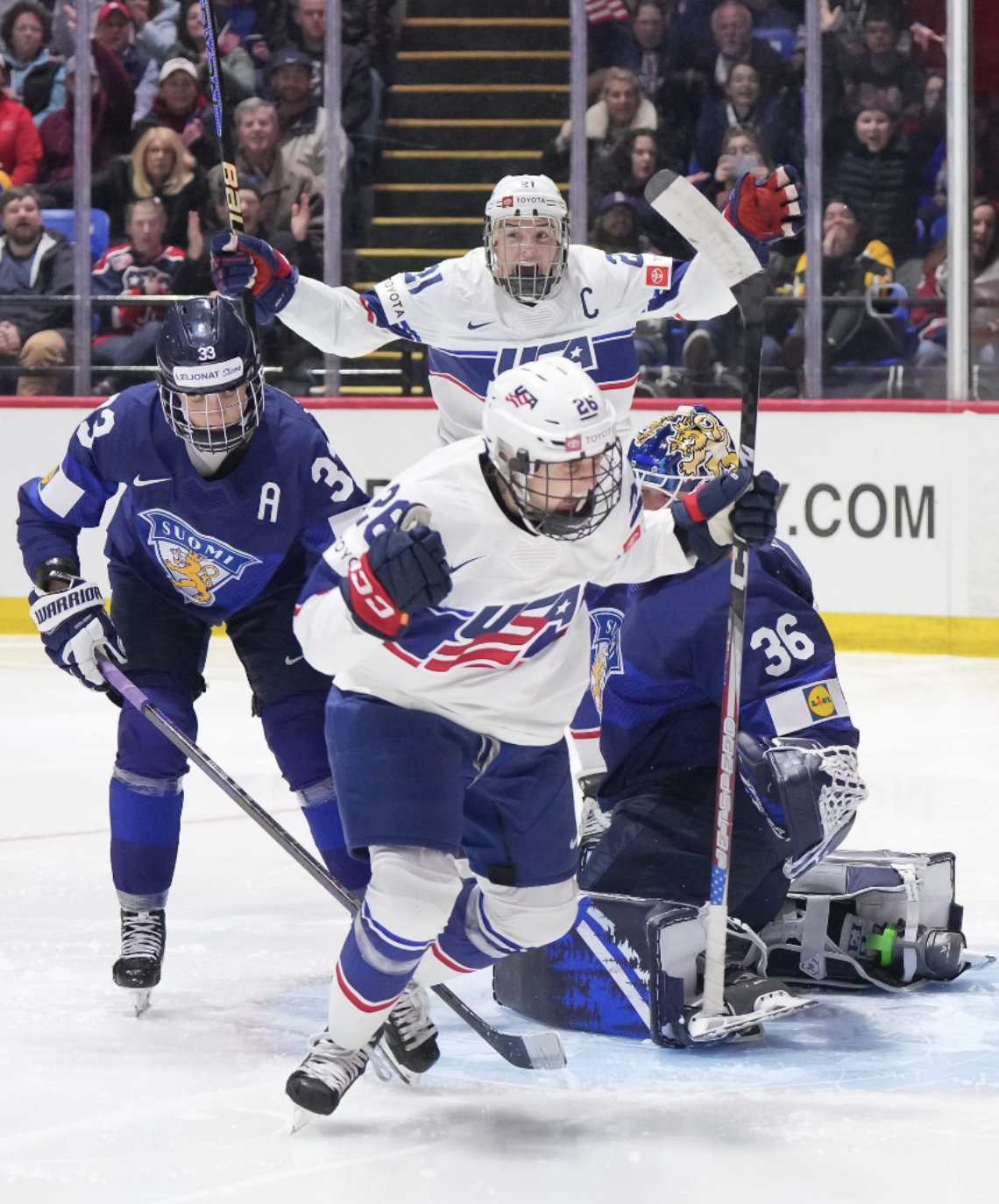 Coyne Schofield pumps her fists and yells in celebration of her goal, while an elated Hilary Knight raises her arms and yells in the background..