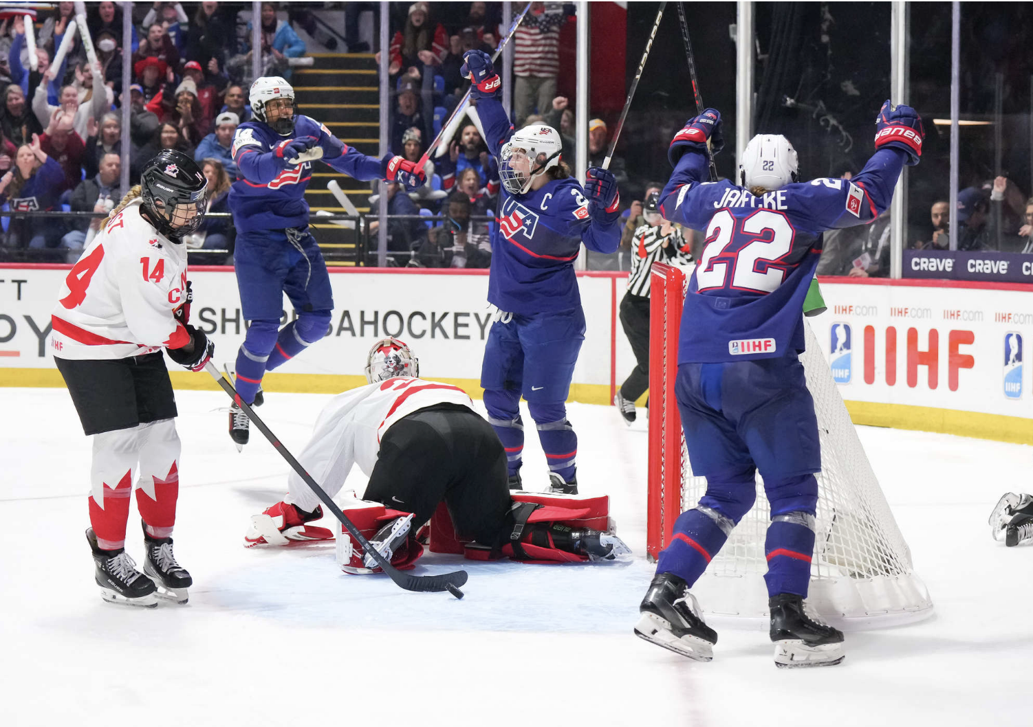 Knight (center, arms raised) celebrates her goal with Edwards (left, jumping) and Janecke (right, coming around the net with arms raised). Renata Fast and Ann-Renée Desbiens look on. The U.S. players are in blue, while Canada is in white.