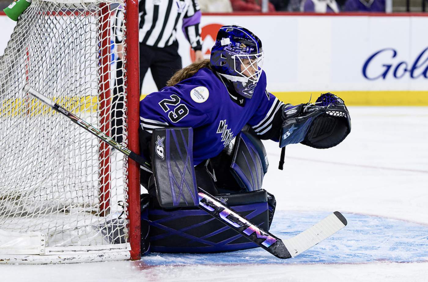 Hensley prepares to make a save from her knees against Boston. She is wearing black and purple goalie gear, and a purple mask and home uniform.