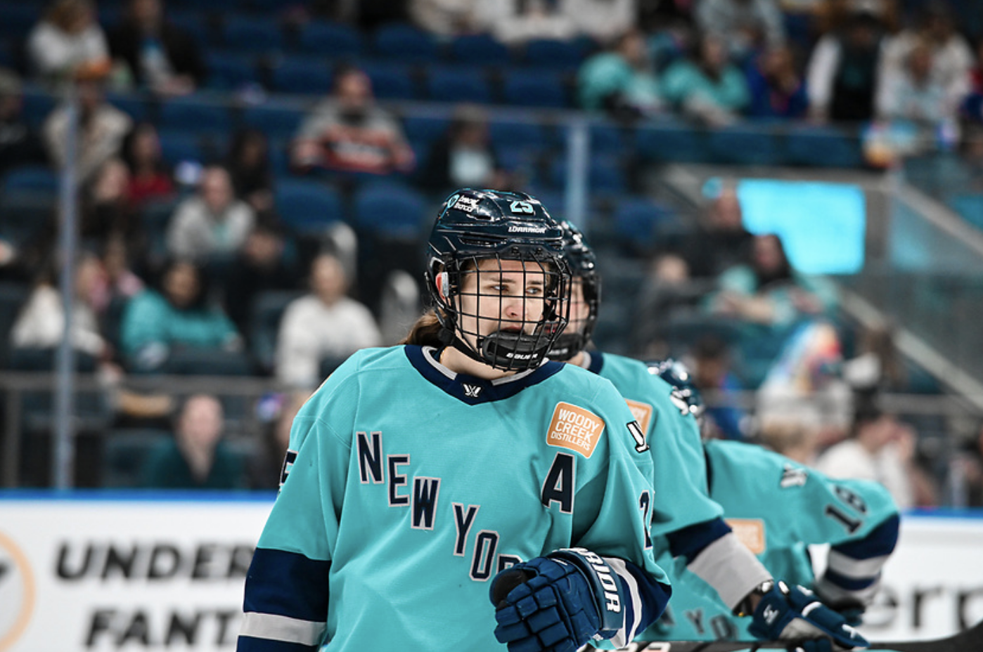 A waist-up shot of Carpenter looking on before a face-off. She is wearing a teal home uniform. 