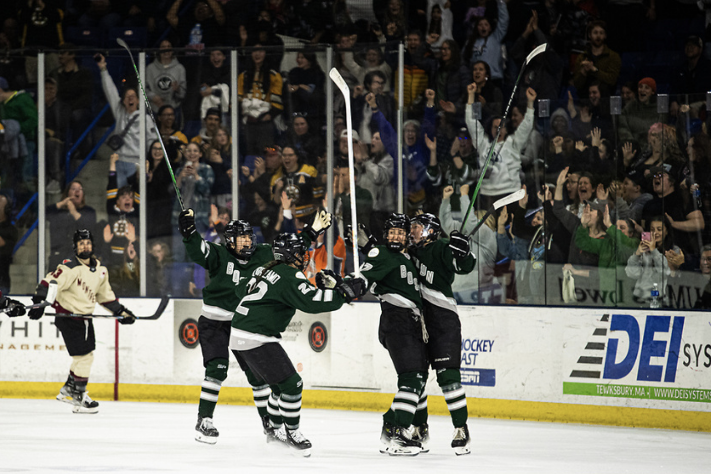 Three Boston players rush to hug Fratkin (right) after her goal against Montréal. They're all smiling and wearing green home uniforms.