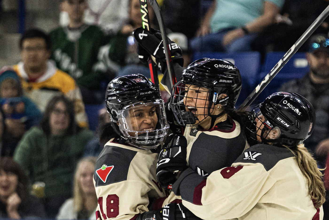 Three Montréal players celebrate a goal with a group hug. They're all smiling and wearing cream away uniforms.