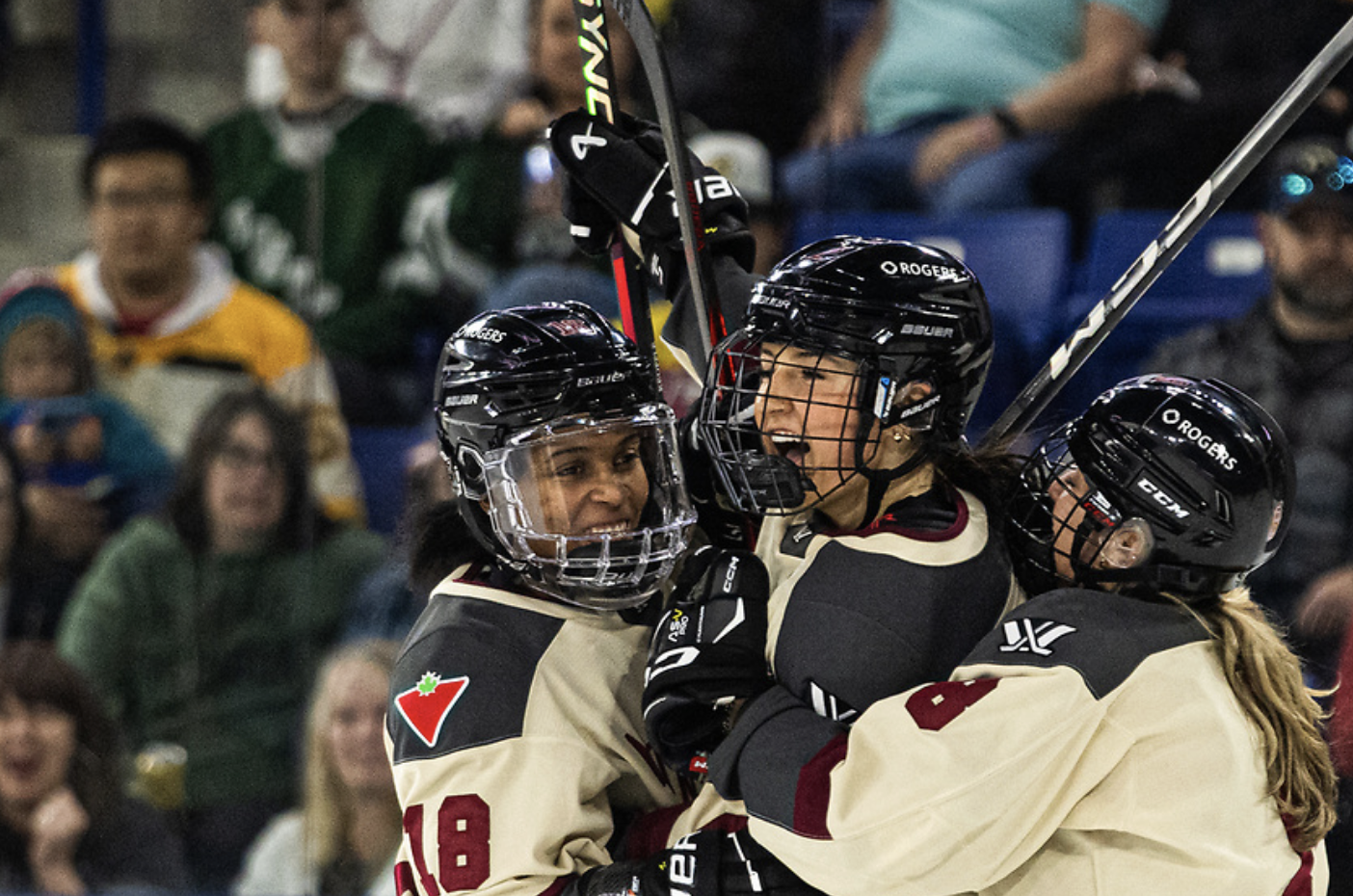 Three Montréal players celebrate a goal with a group hug. They're all smiling and their sticks are raised up between them. They're wearing cream away uniforms.