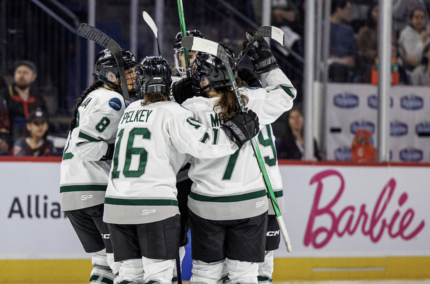 Five Boston players celebrate a goal with a group hug. They're all raising their sticks and are wearing white away uniforms.