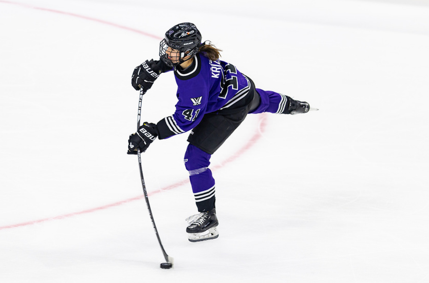 Denisa Křížová transfers all her weight to her front foot while flexing her stick. She is about to take a shot. She is wearing a purple home uniform.