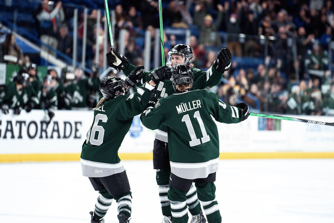 Keller celebrates her goal with a group hug with Müller and Gabel. They're all wearing green home uniforms.