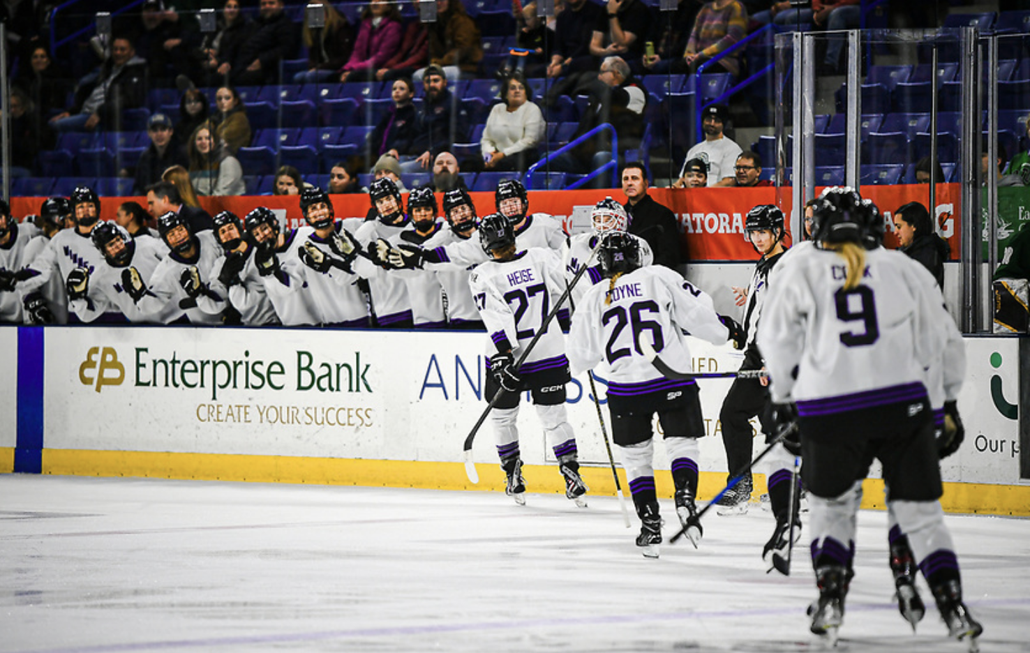 Five Minnesota players celebrate a goal by going down a handshake line at the bench. They're wearing white away uniforms.