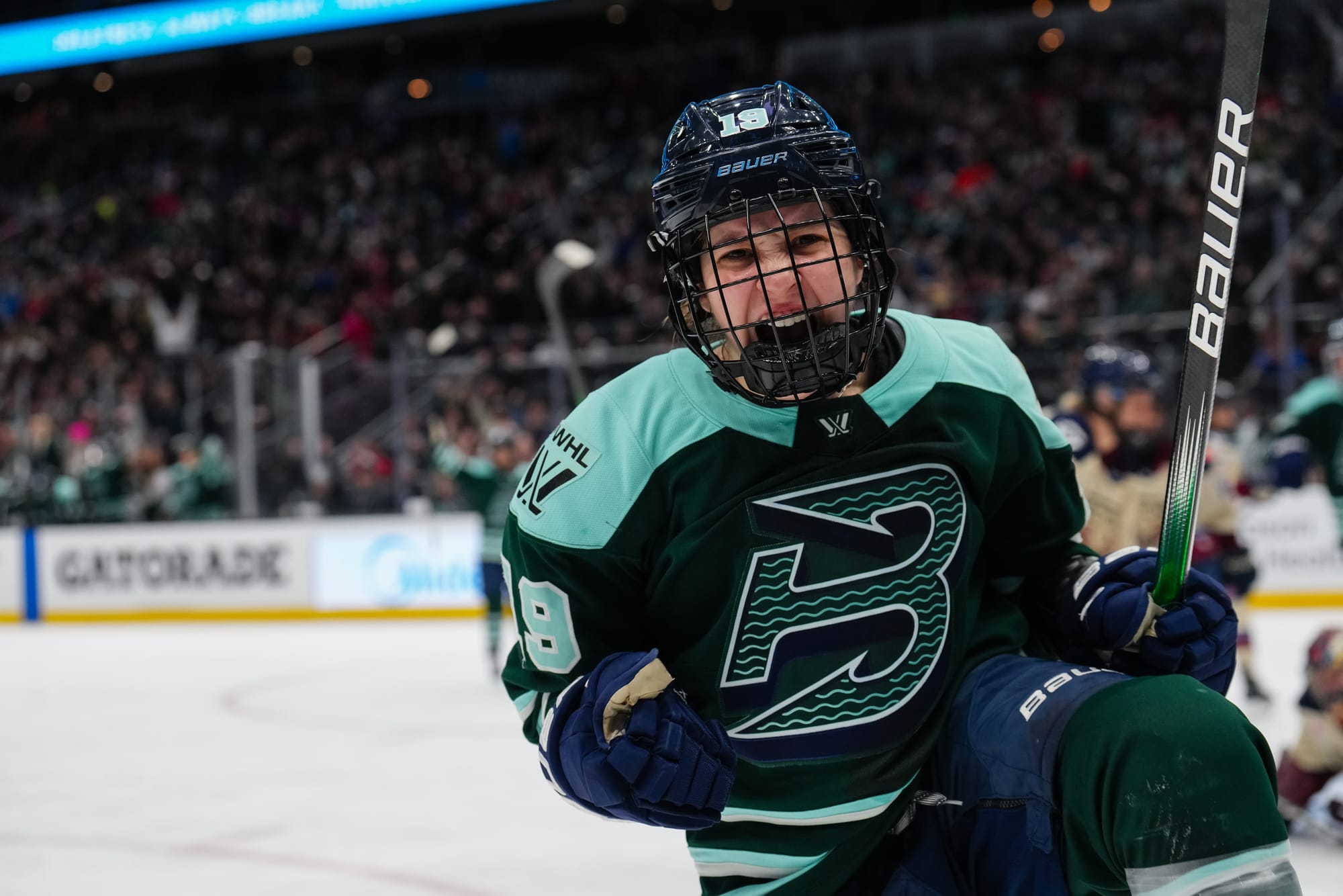 Bilka looks at the camera, pumps her fists while raising her left leg, and yells while smiling. She is wearing a green home uniform.