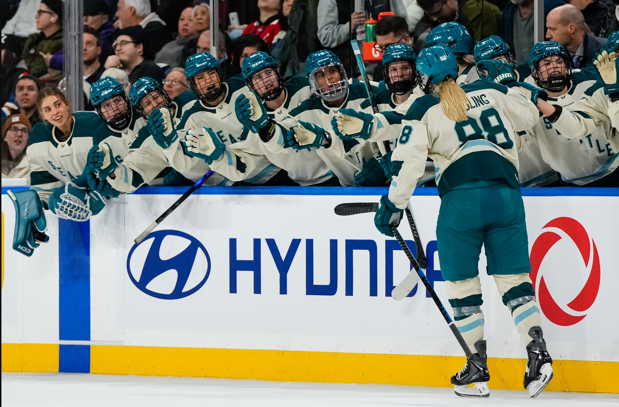 Gosling goes down the bench line, getting fist bumps from her teammates in celebration of a goal. They are all wearing cream away uniforms.