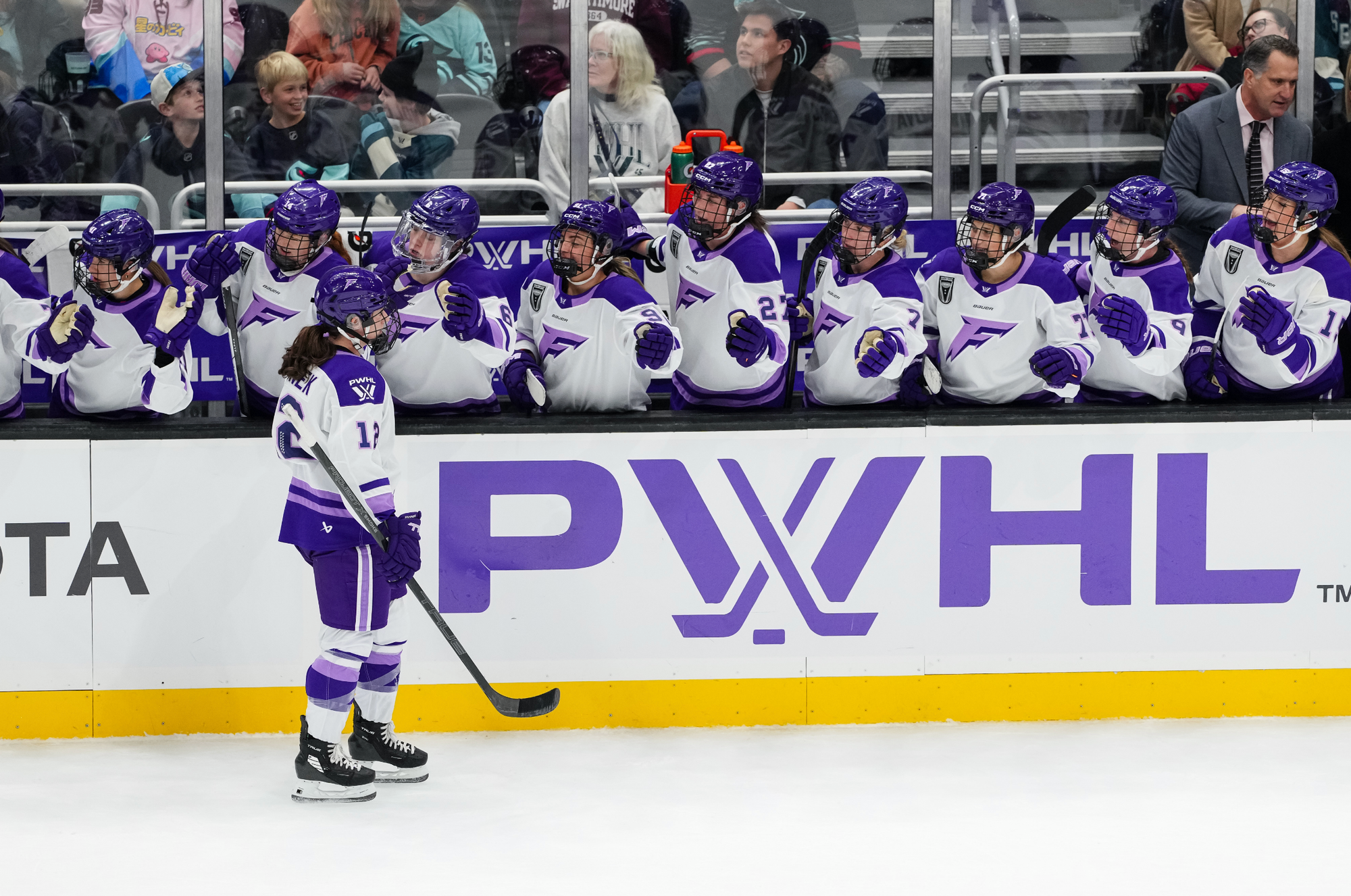 Pannek skates down the handshake line at the bench as her teammates smile and yell in celebration. They are all wearing white away uniforms.