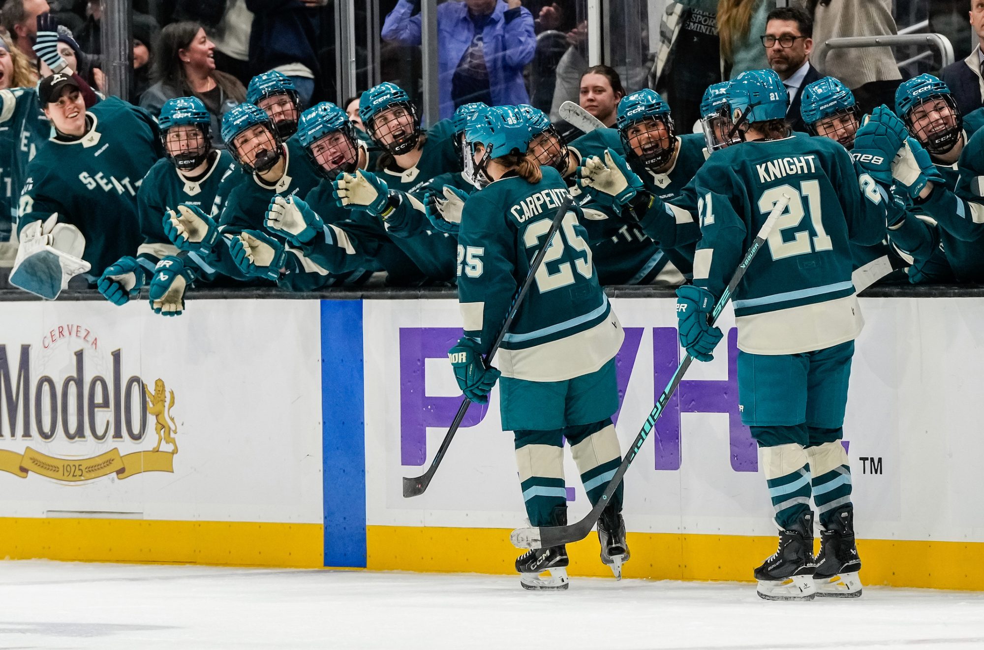 Carpenter and Knight celebrate a goal by going down the handshake line at the bench. They are all wearing teal home uniforms.