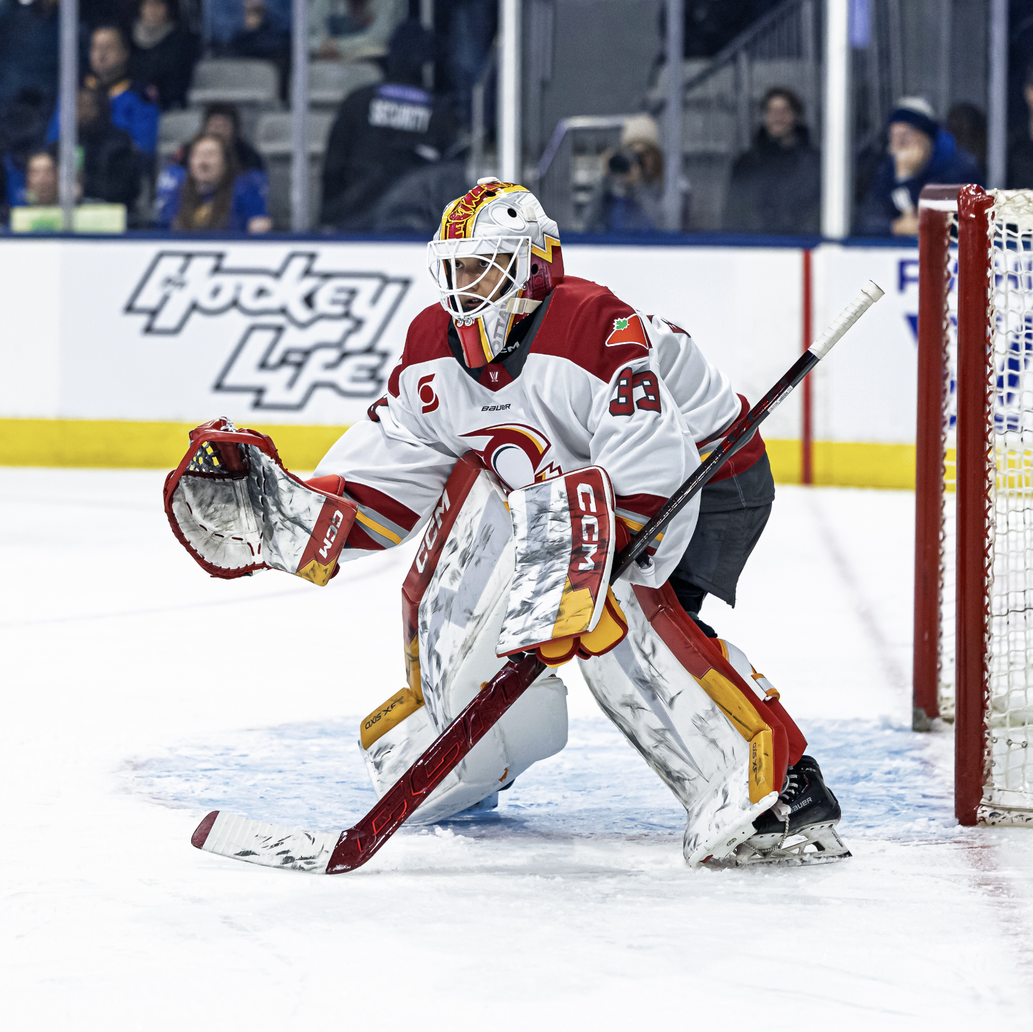 Phillips gets set in a crouched stance as she prepares to make a save. She is wearing a white away uniform and watching the puck, which is out of frame.