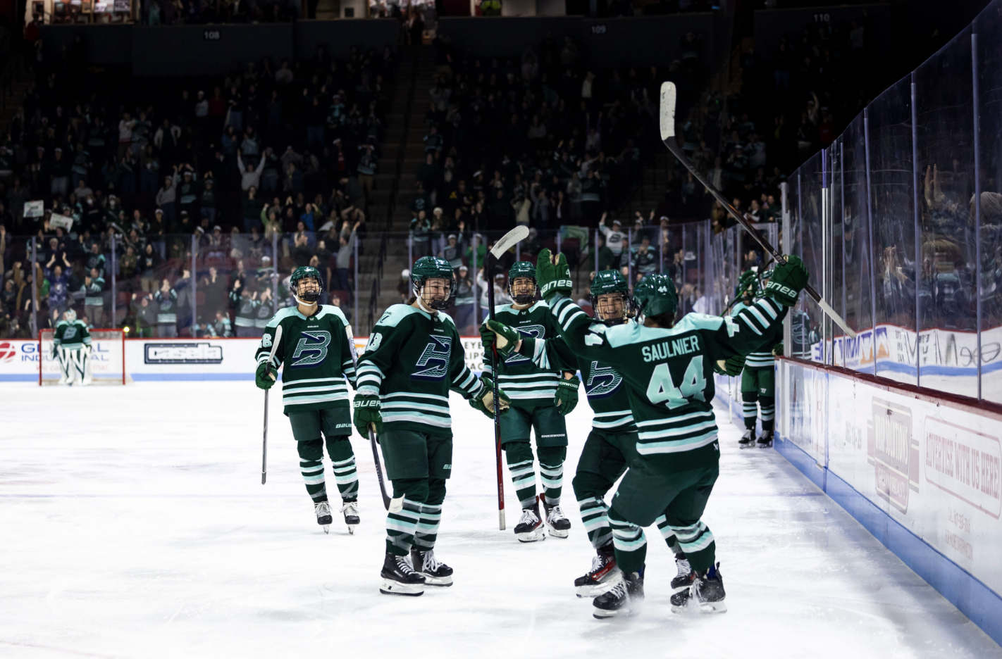 Saulnier skaters toward her teammates with her arms in the air and held wide open for a hug. They are all wearing green home uniforms.