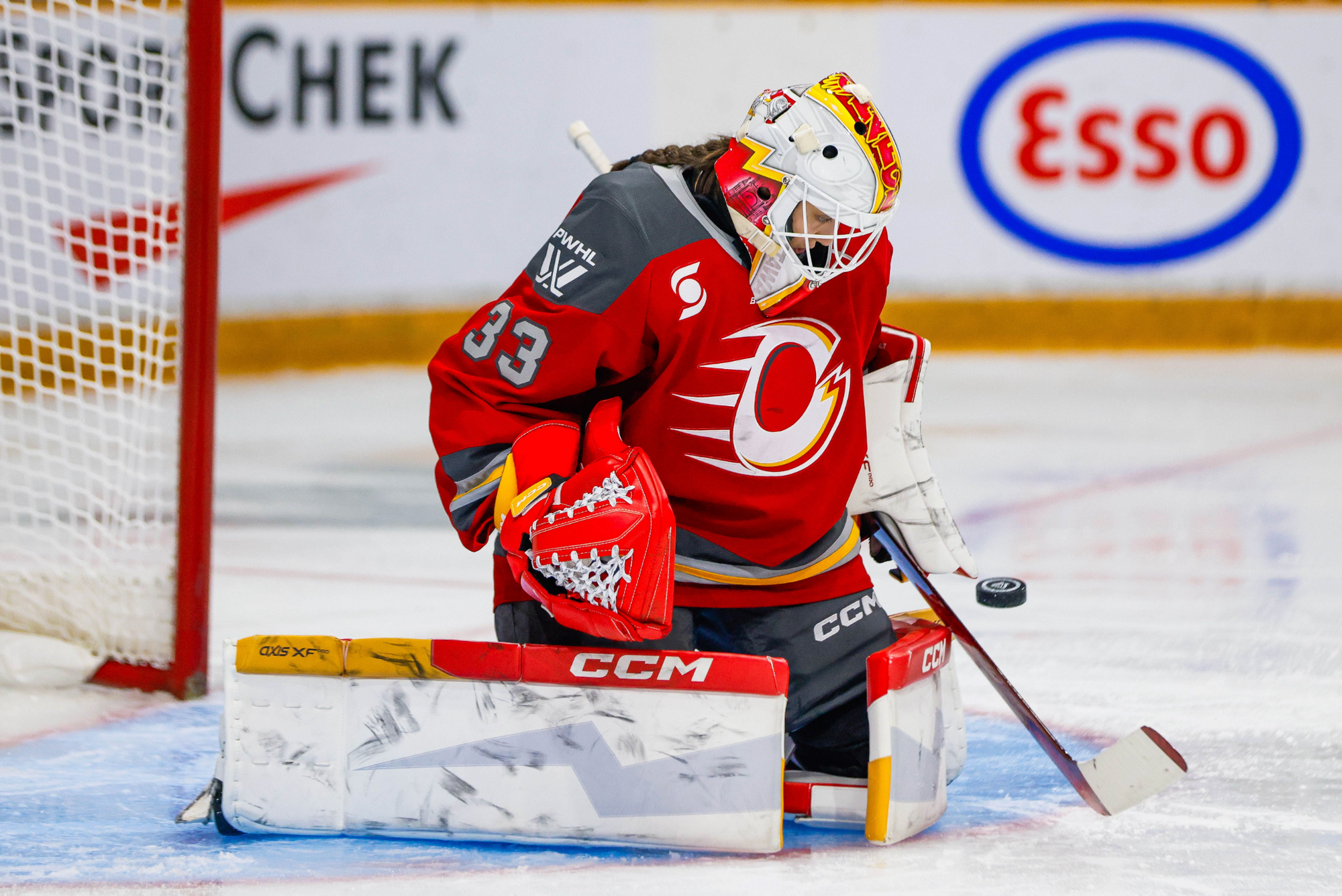 From her knees, Phillips kicks out a puck from her crease. She is wearing a red home uniform.