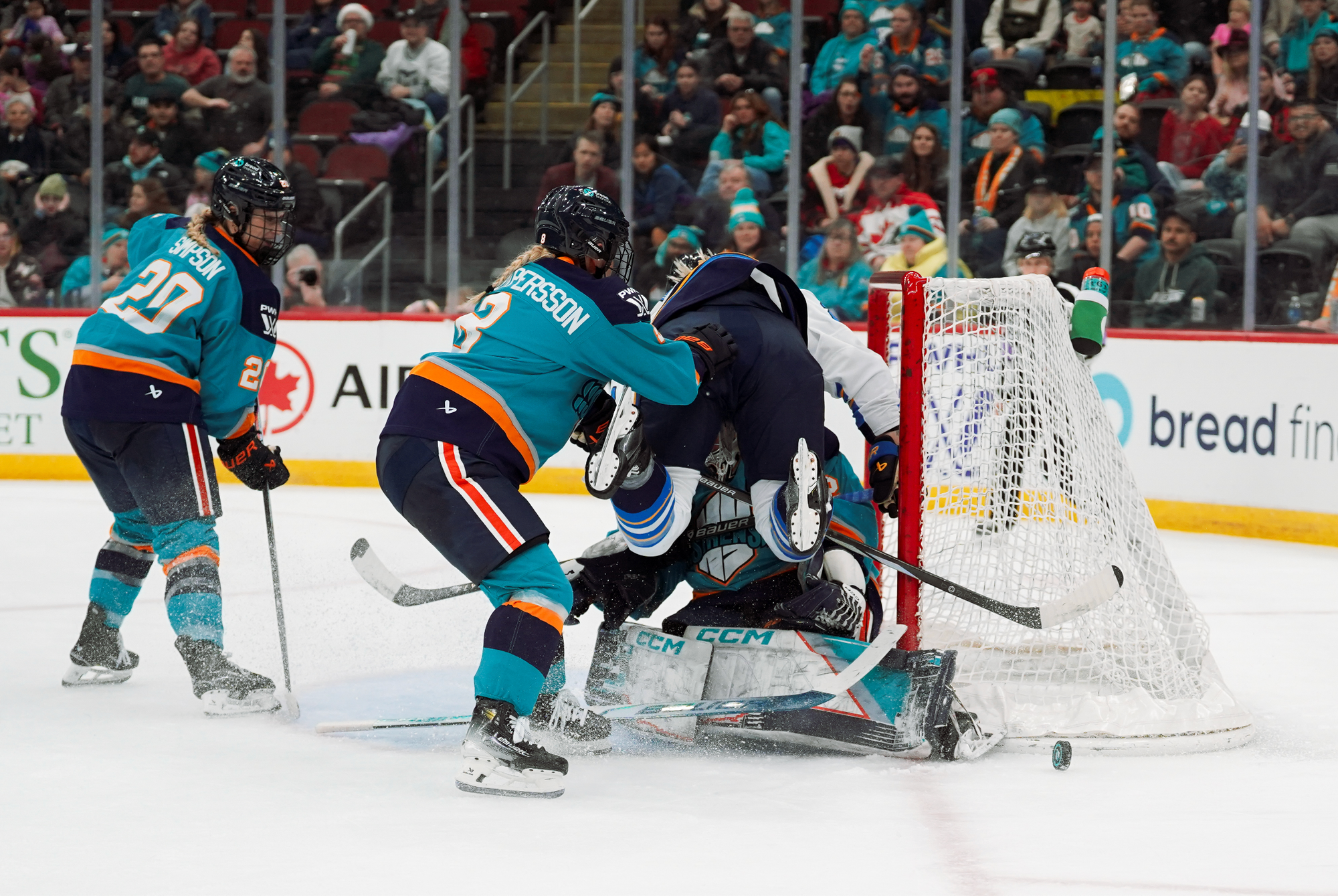 Nylén-Persson appears to shove the Toronto player, who is in the air and about to make contact with Osborne, who is on her knees in her crease. The New York players are in teal home uniforms, while the Toronto player is in a white away one.
