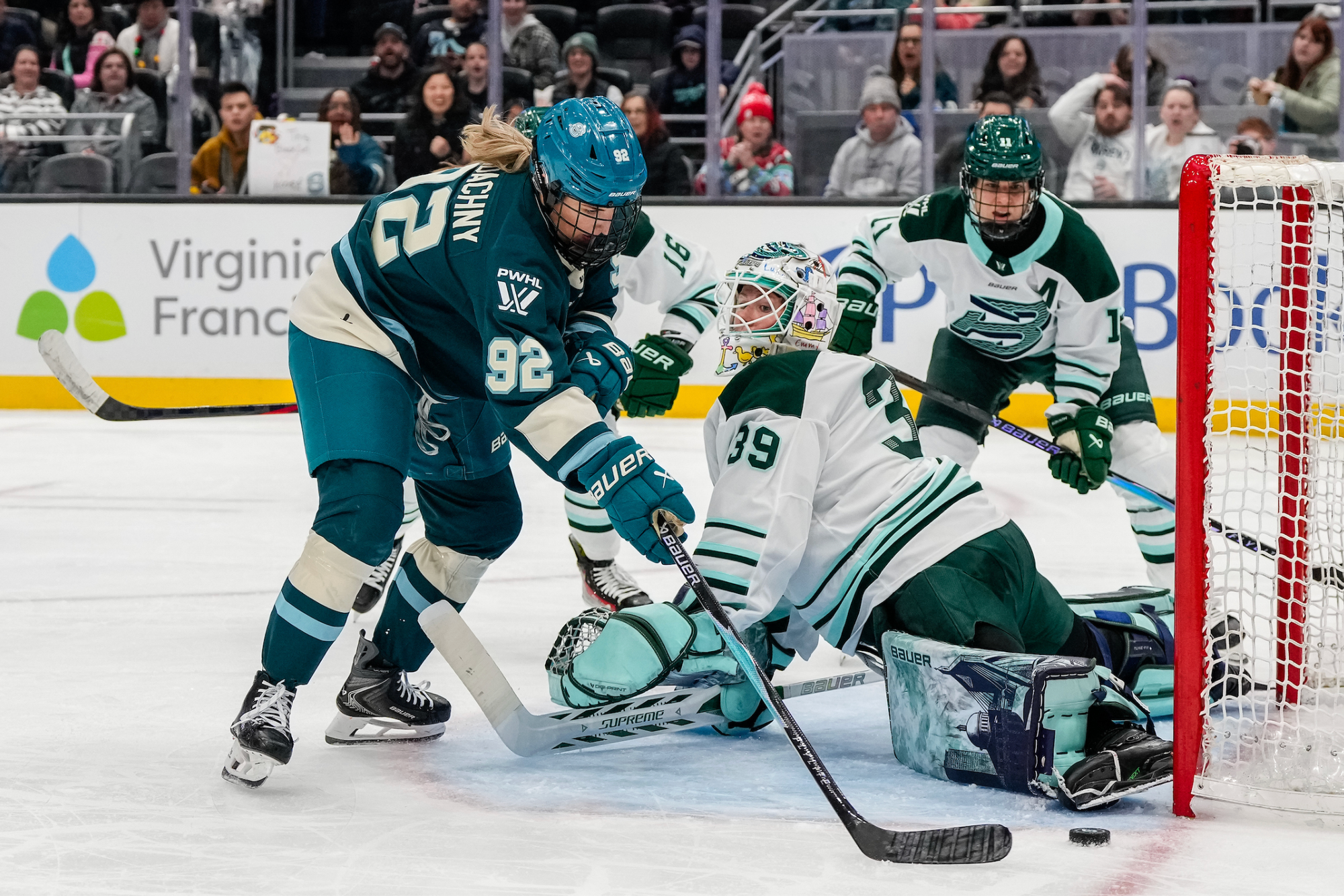 Serdachny tries to reach around a sprawling Levy to score as Boston players try to defend. She is wearing a teal home uniform, while Levy and her teammates are in white away ones.