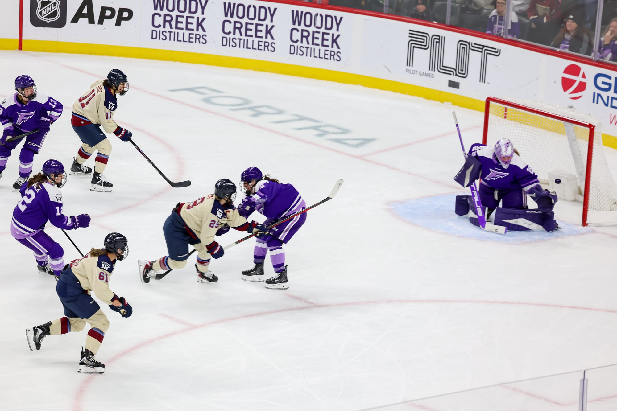 Flanked by her teammates and while a Minnesota defender tries to stop her, Poulin sends a highlight-reel goal past Hensley, who is on her knees trying to make the save. The Victoire players are in cream away uniforms, while the Frost are in purple home ones.