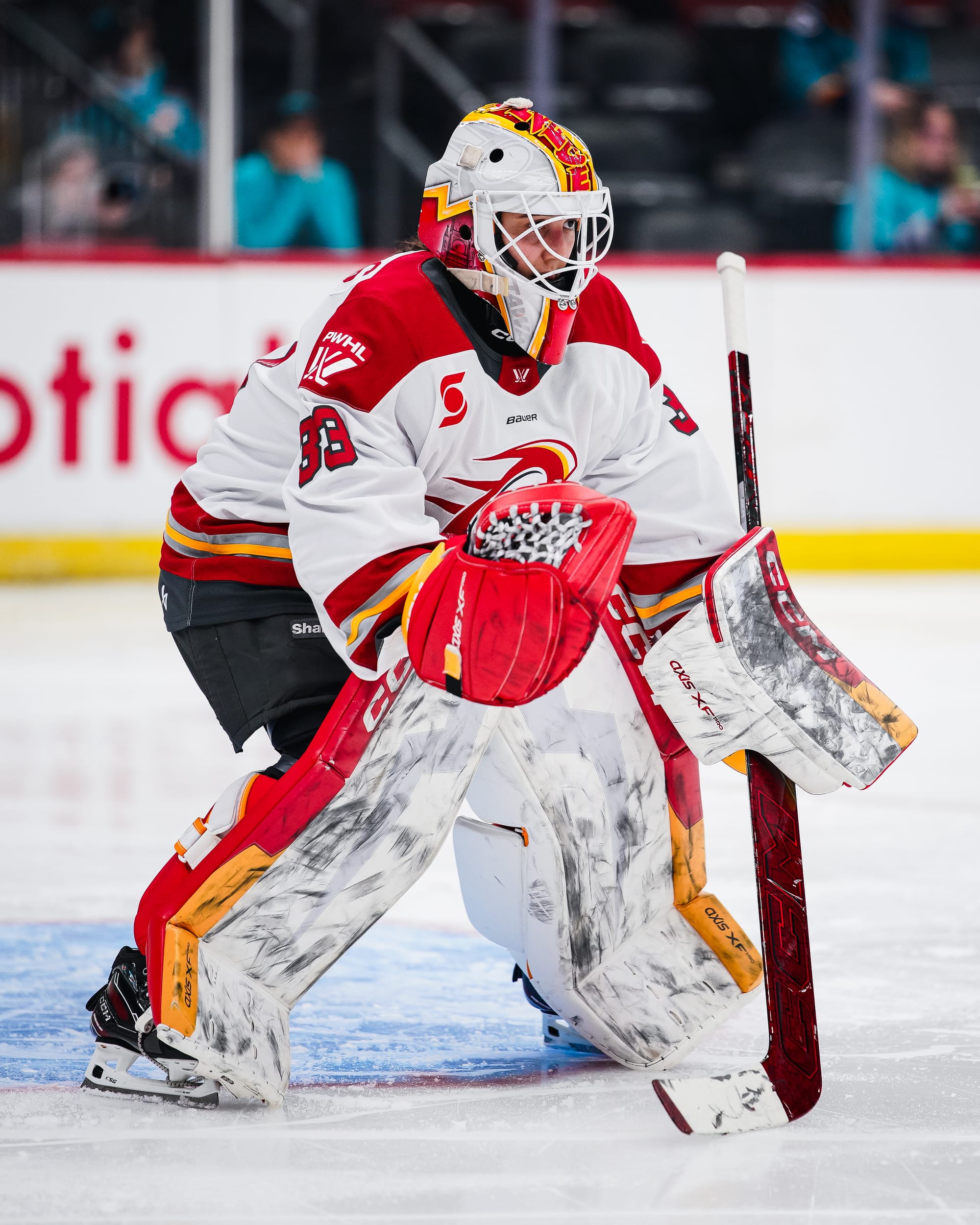 Phillips is in the standard goalie position, slightly crouched, with her stick on the ice and her glove down low. She is wearing a white away uniform.