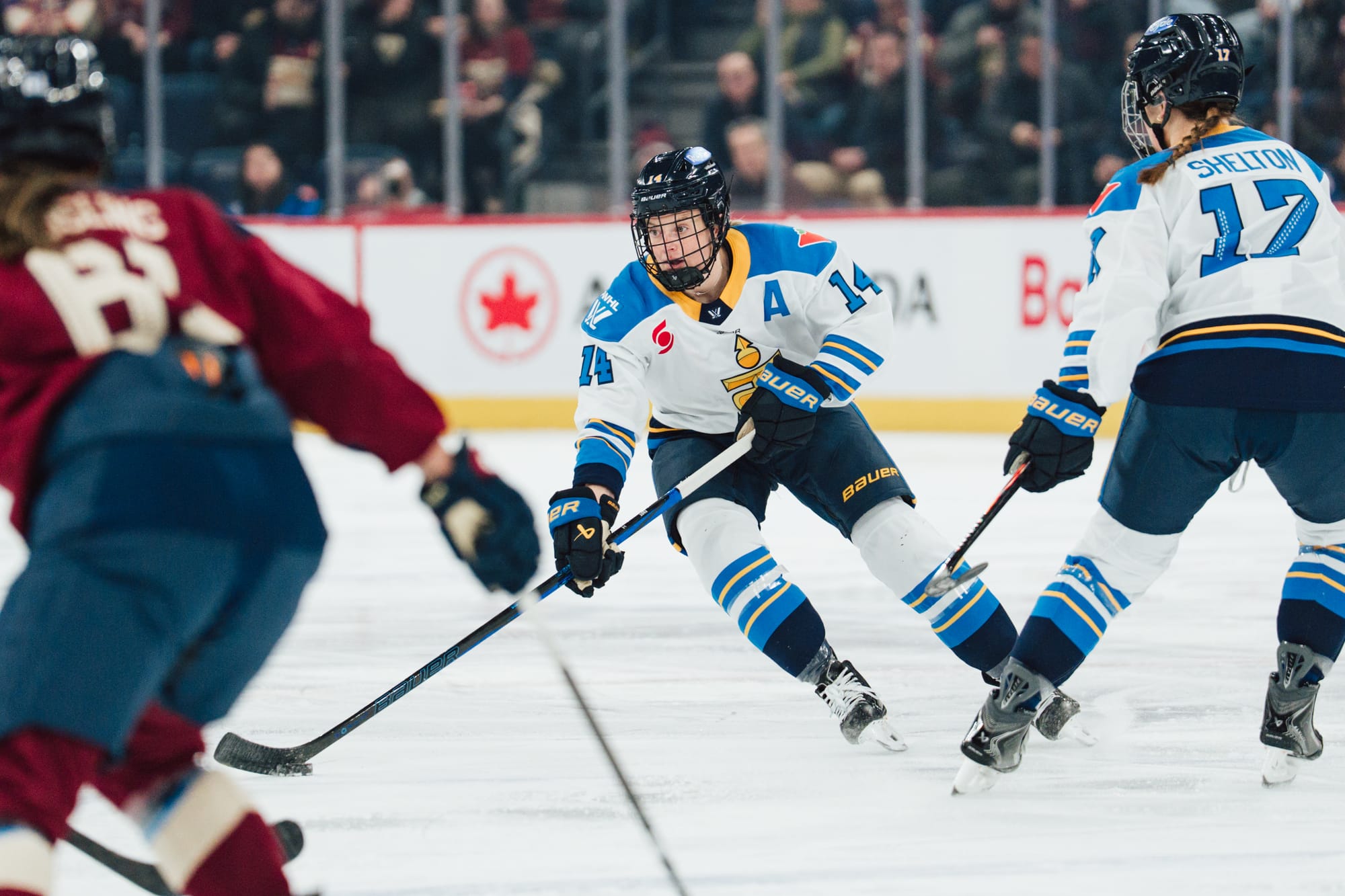 Fast skates up ice with the puck. She is wearing a white away uniform.